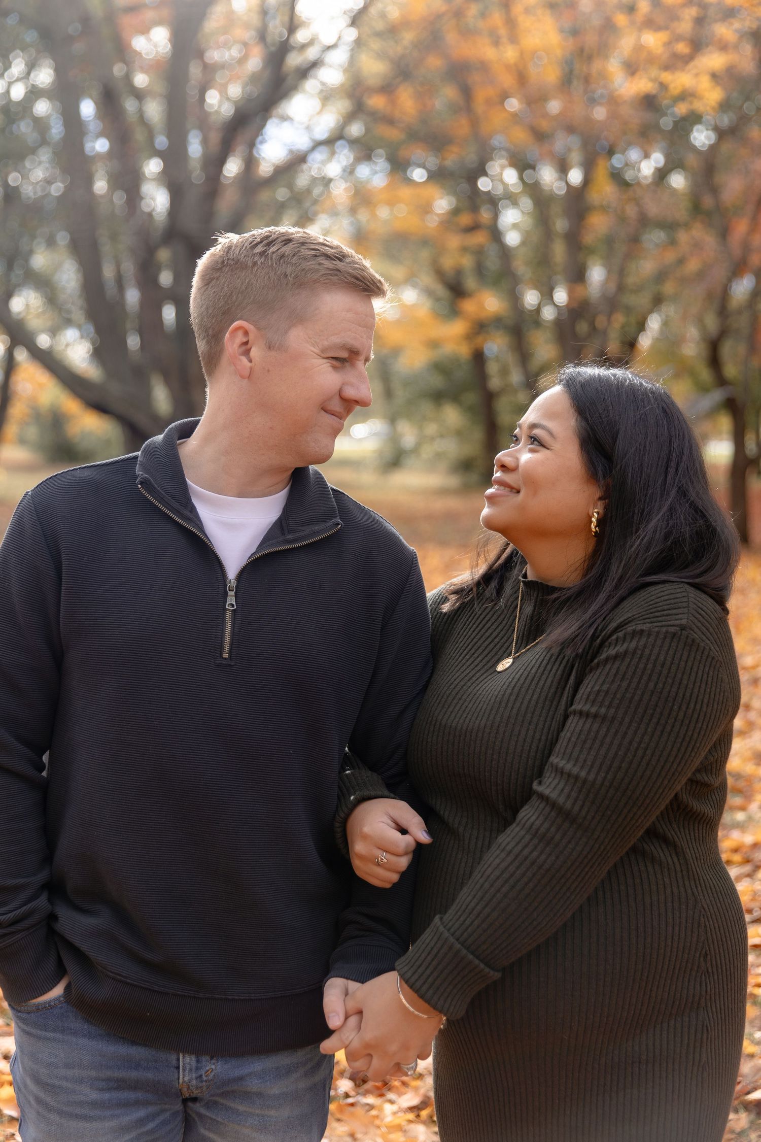 A couple in matching black and white outfits share a tender moment among autumn leaves in a park setting.