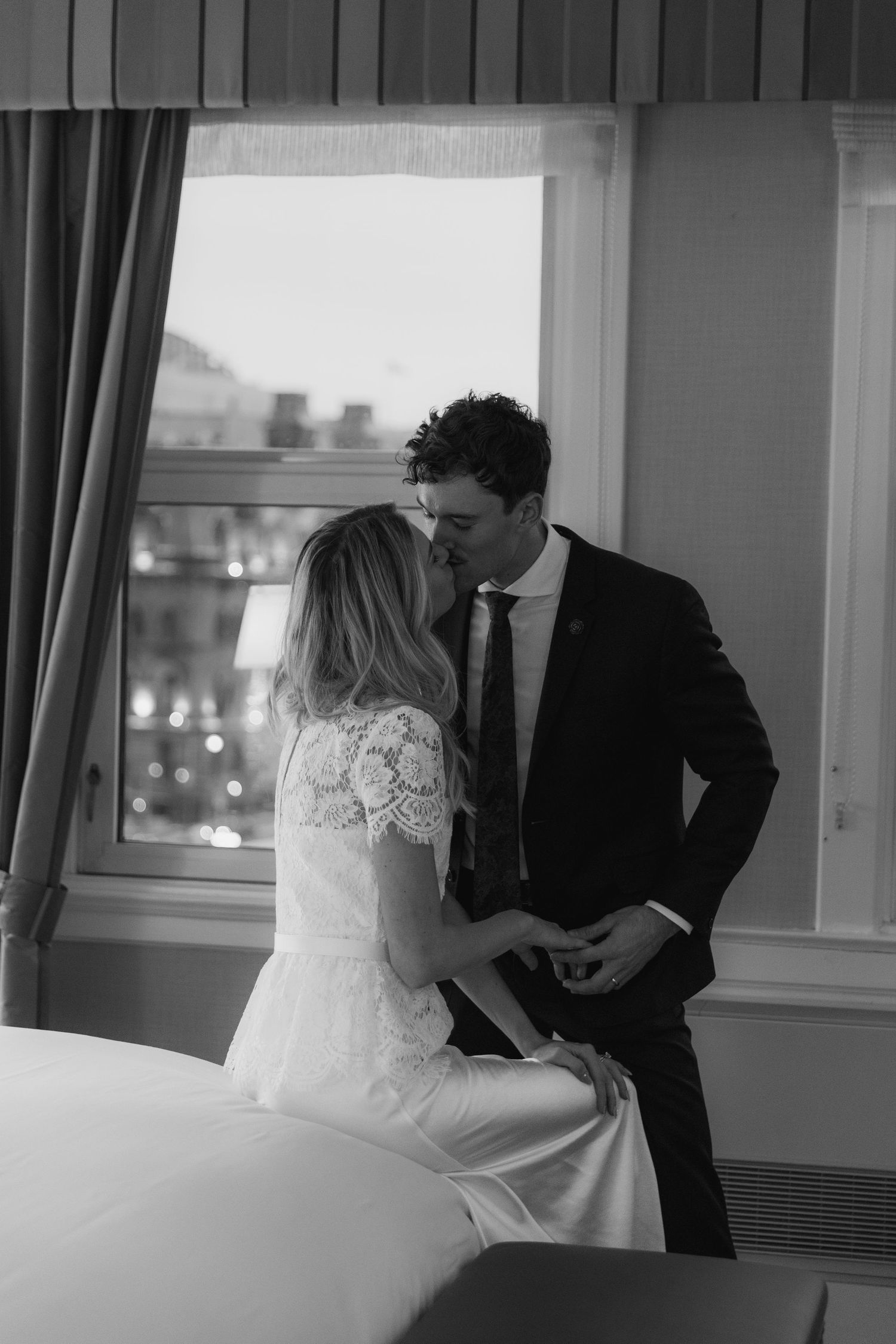 Black and white photo of a bride and groom sharing an intimate moment by a window on their wedding day.