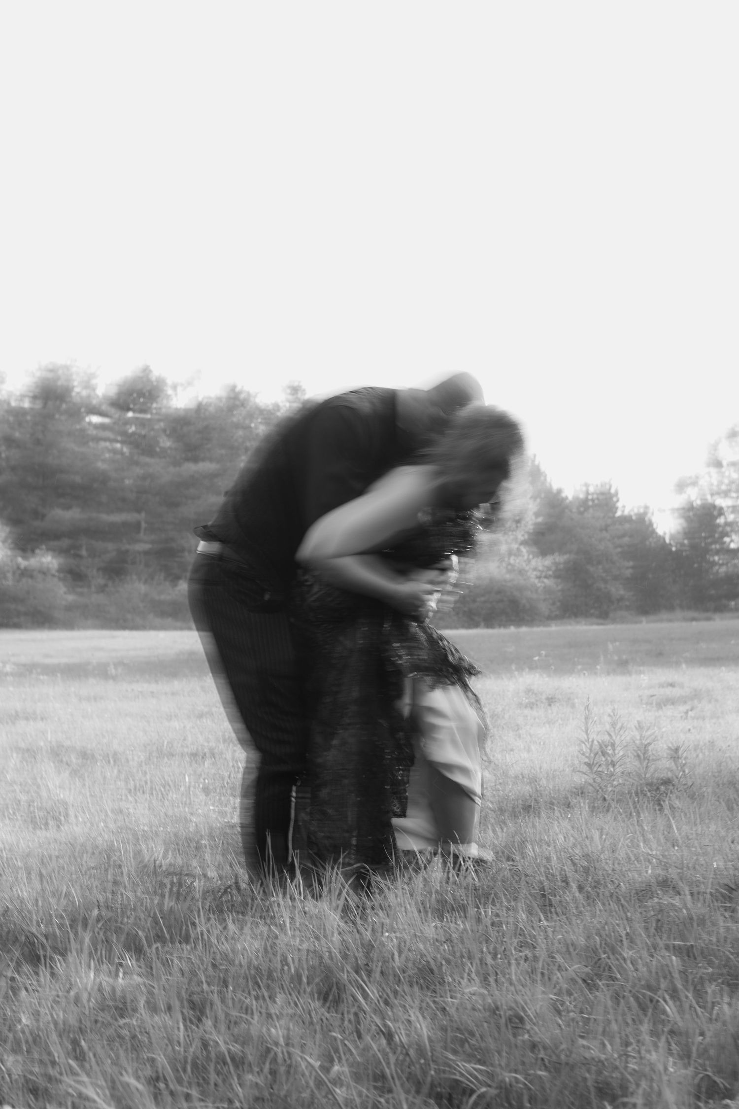 A blurred black and white artistic photograph of two people embracing in a grassy field.