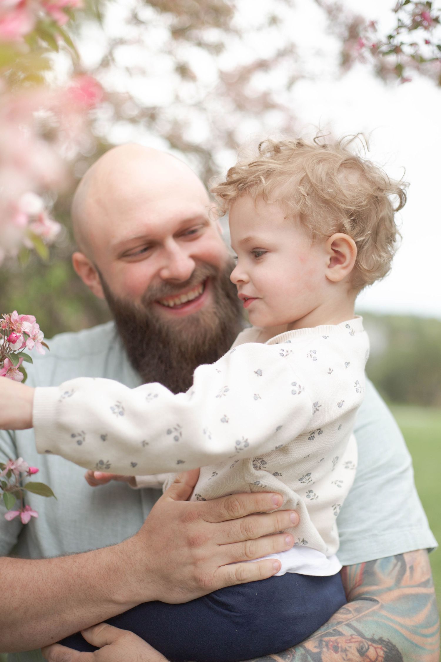 A parent and small child share tender moments under blooming cherry blossoms in spring.