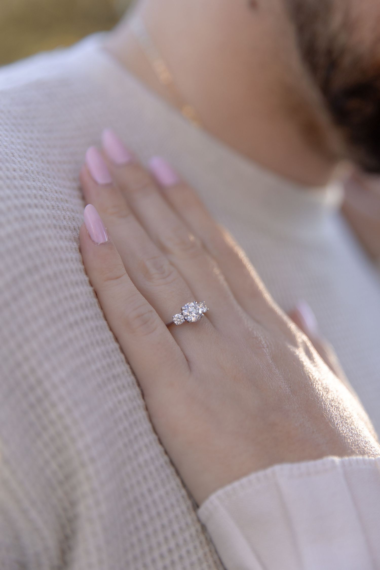 A close-up sequence of a hand wearing a white sweater showing off a sparkling engagement ring in natural light.