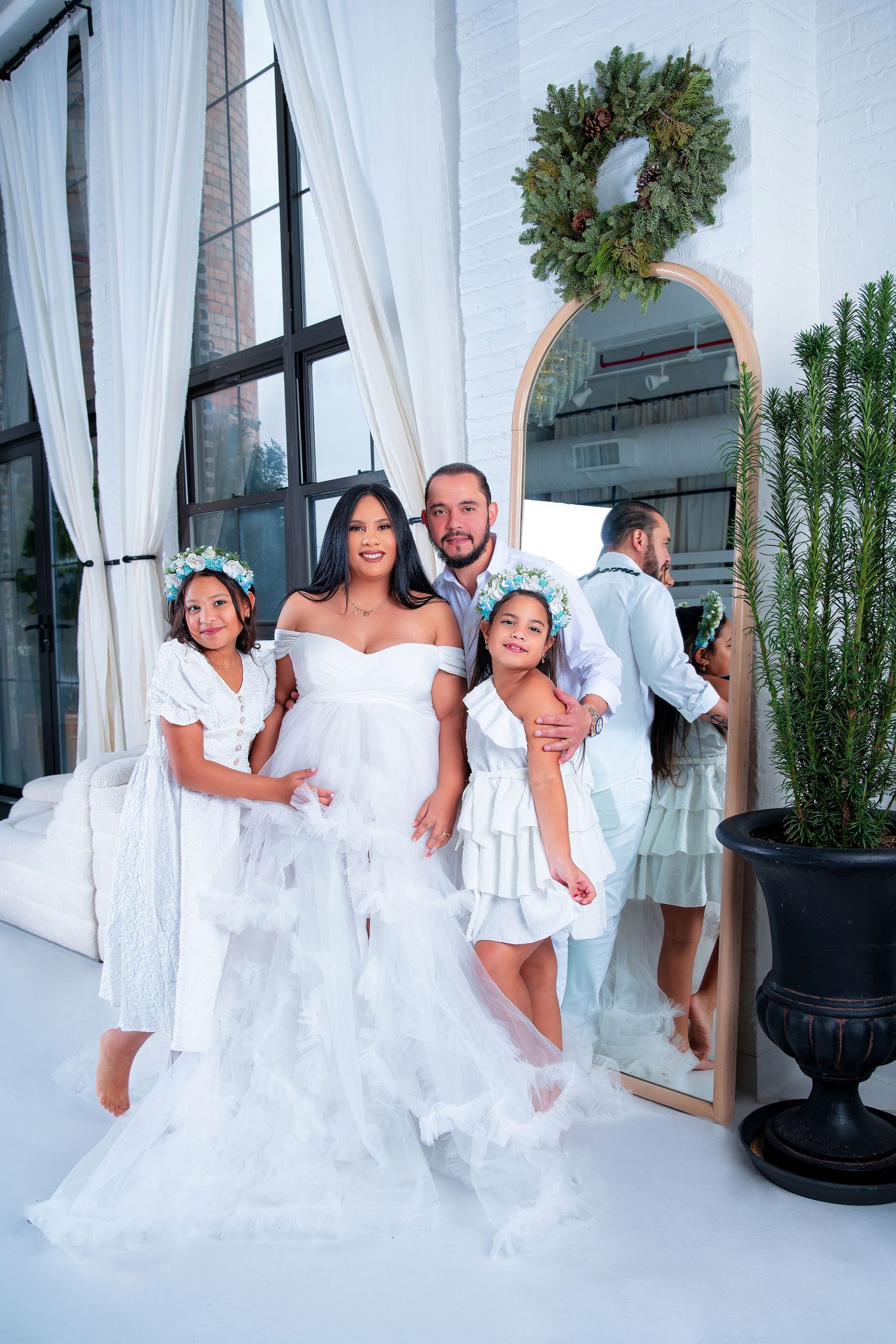 A wedding party in white attire poses elegantly in front of a decorative mirror with a holiday wreath.