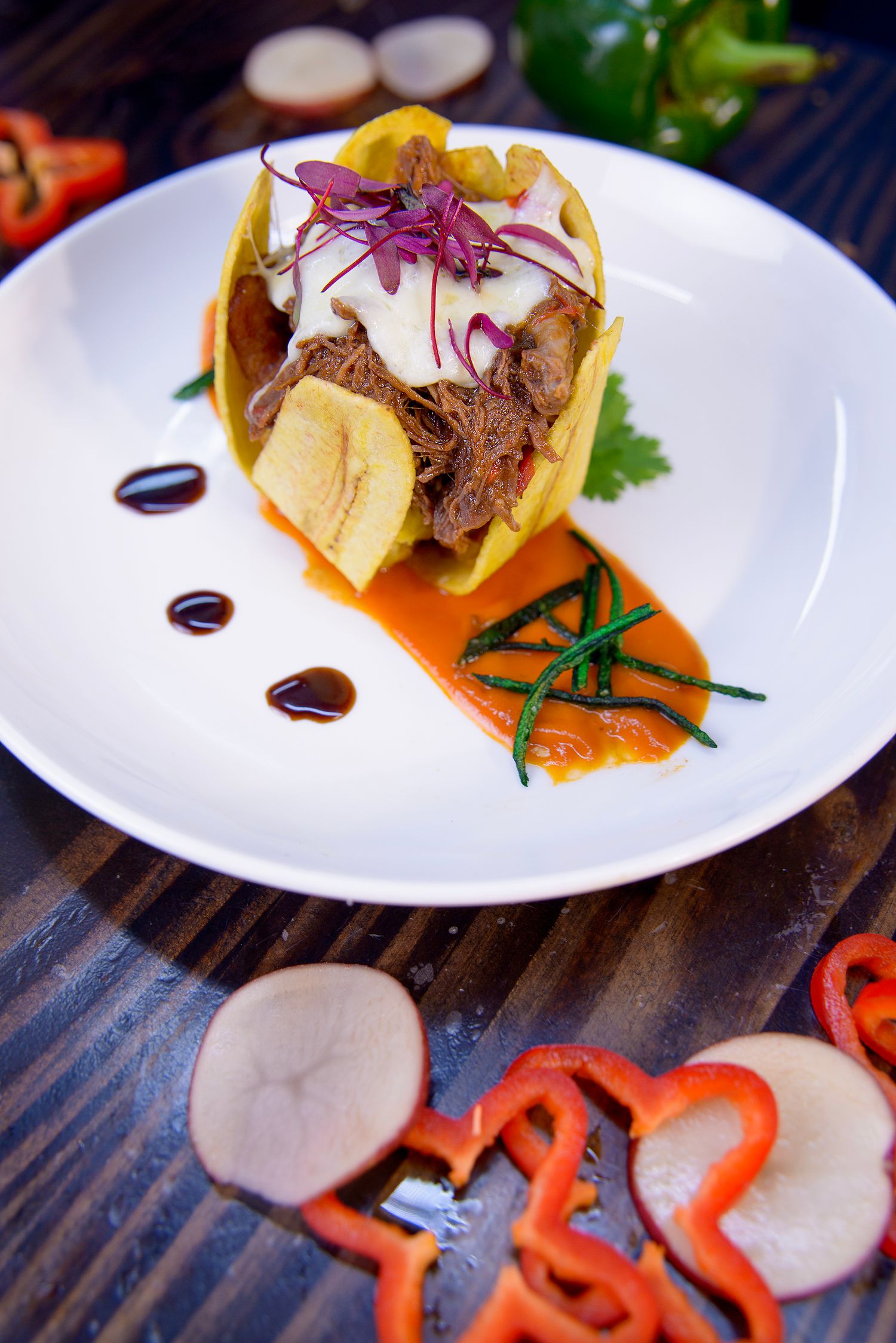 Gourmet taco served on white plate with red onions and decorative sauce drizzle.