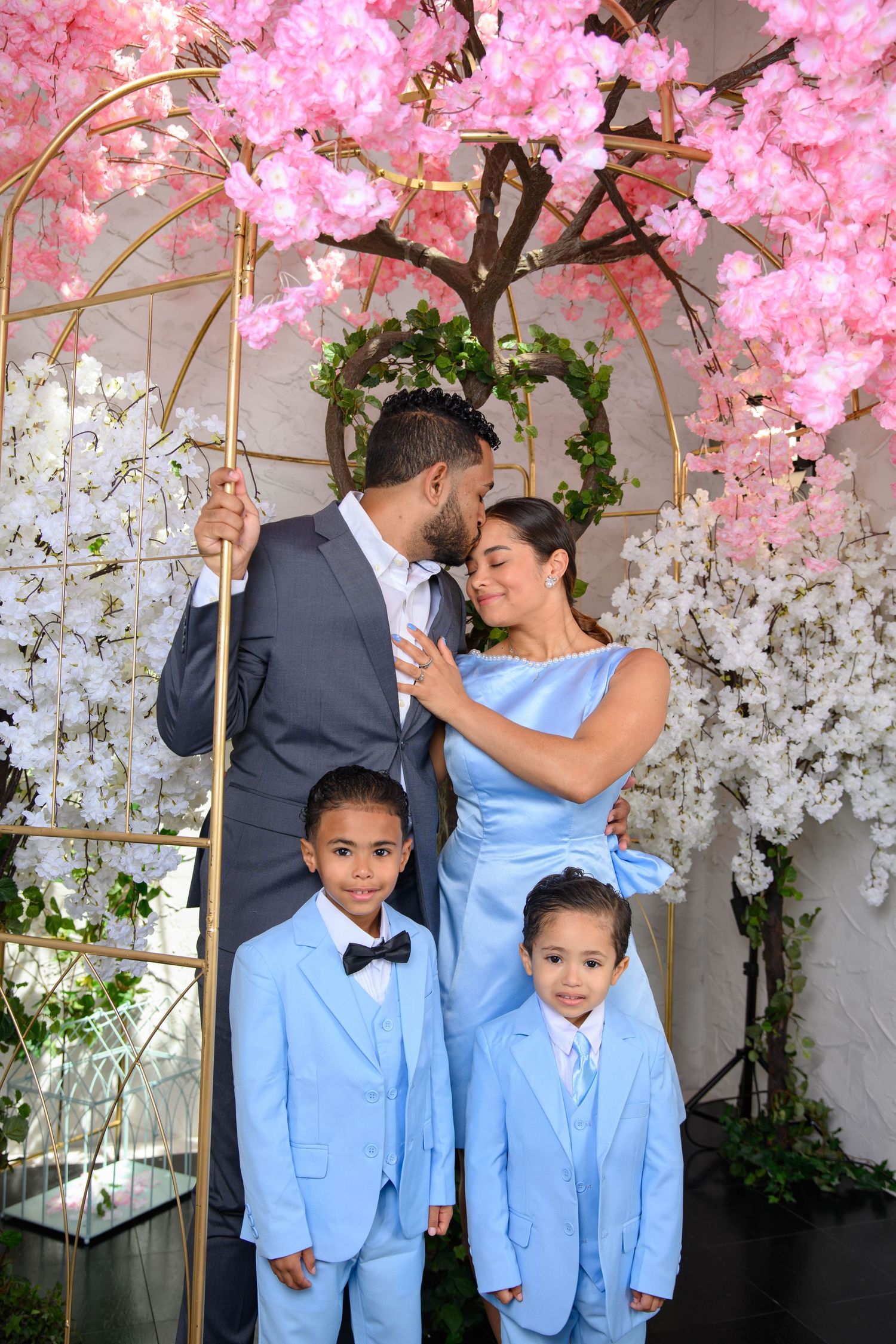 Family in coordinating light blue outfits pose together under beautiful pink and white cherry blossom trees.