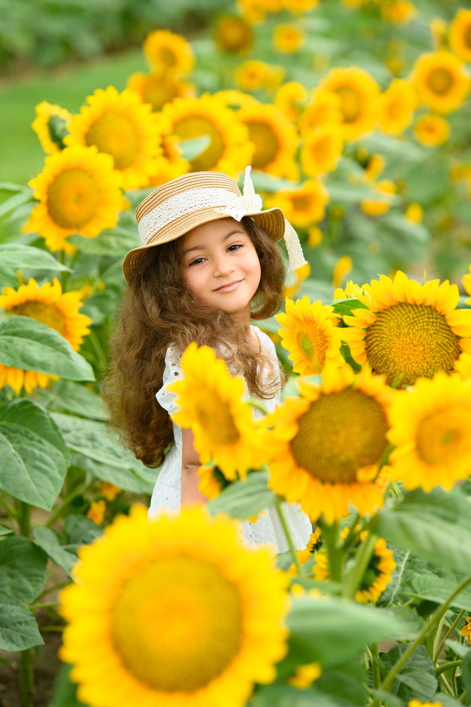 A charming portrait among bright yellow sunflowers with someone wearing a straw hat and white dress.