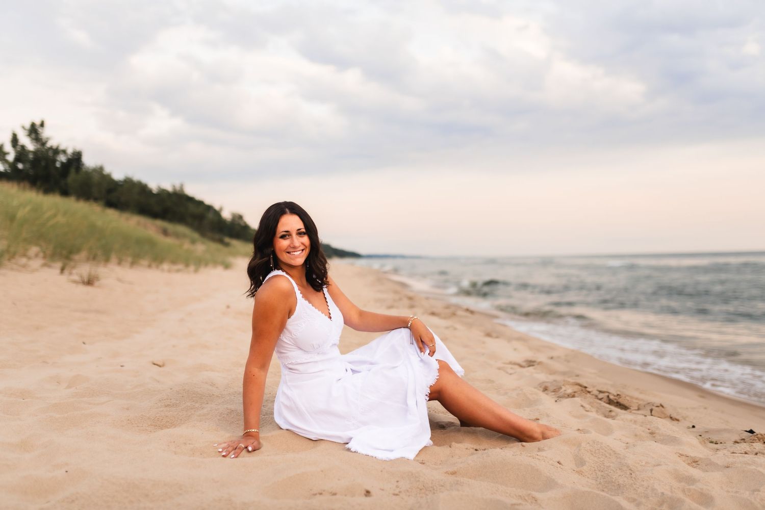 Portrait of a senior girl, sitting at Hoffmaster Beach with the lake and dune grass behind ber.
