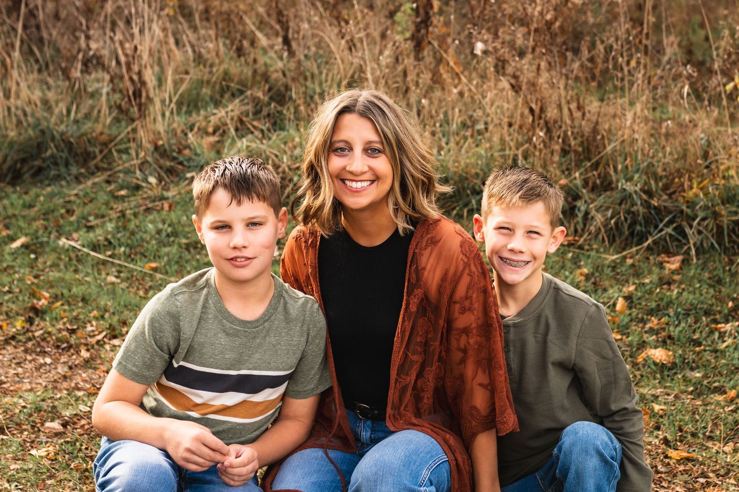 Portrait of a mom with her sons wearing coordinated outfits in a field during golden hour.