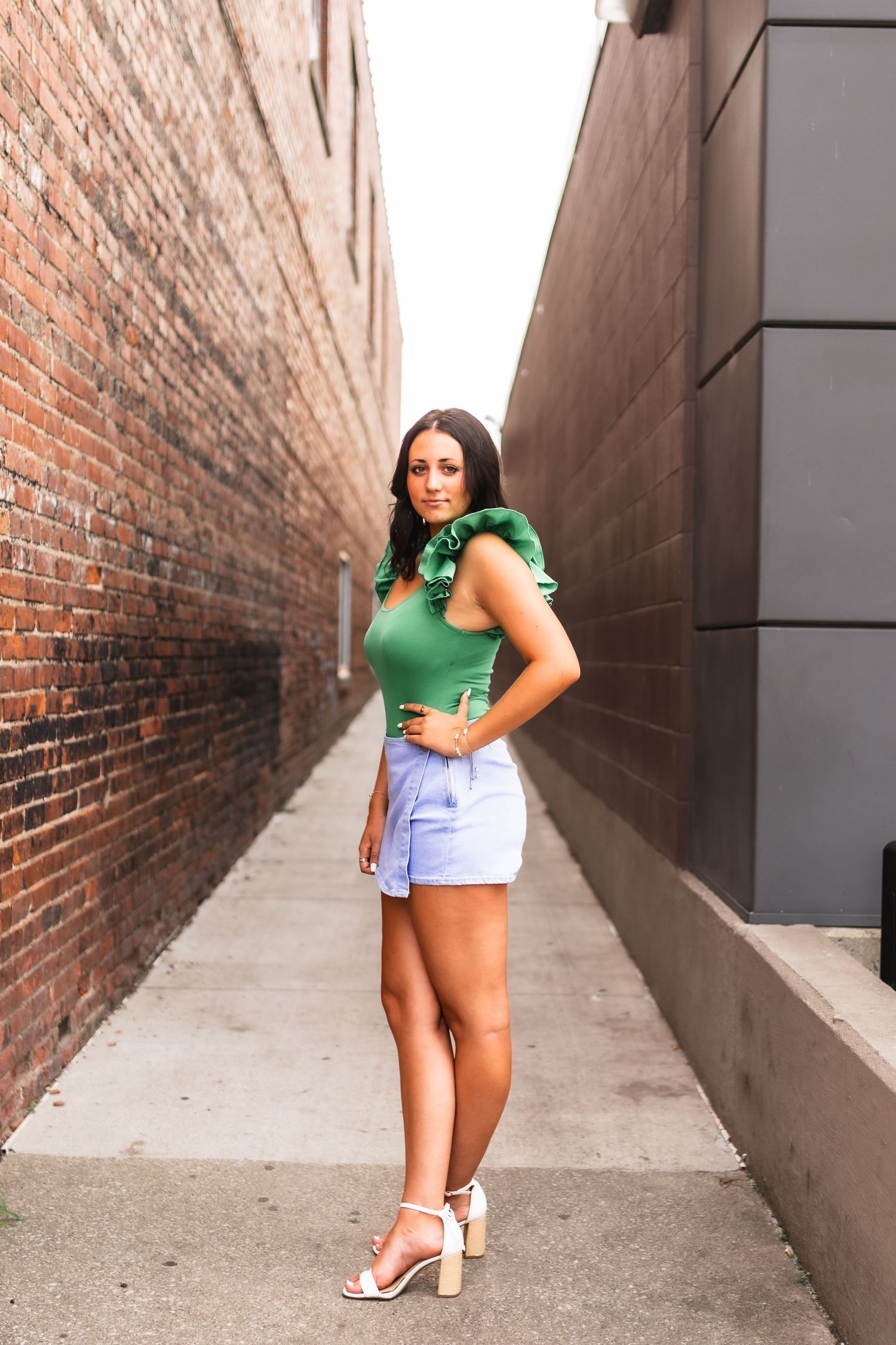 A senior girl in a green blouse and skirt posing in front of an alley in Muskegon MI