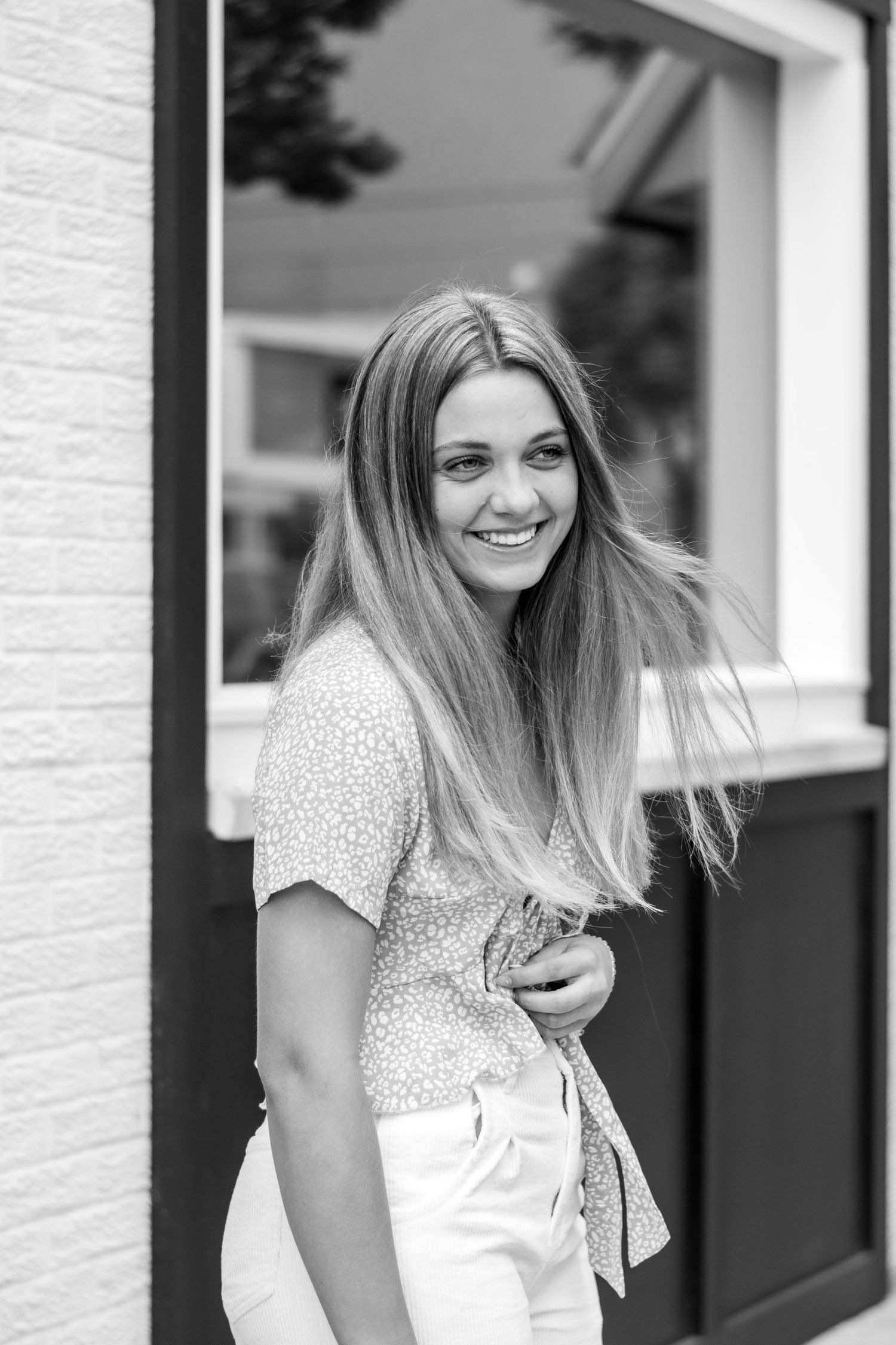 Candid black and white portrait of a senior girl laughing as the wind catches her hair .