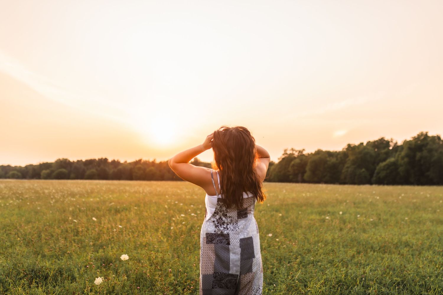 Candid portrait of a girl during her senior session walking away from the camera while fixing her hair, with the sun setting behind her.