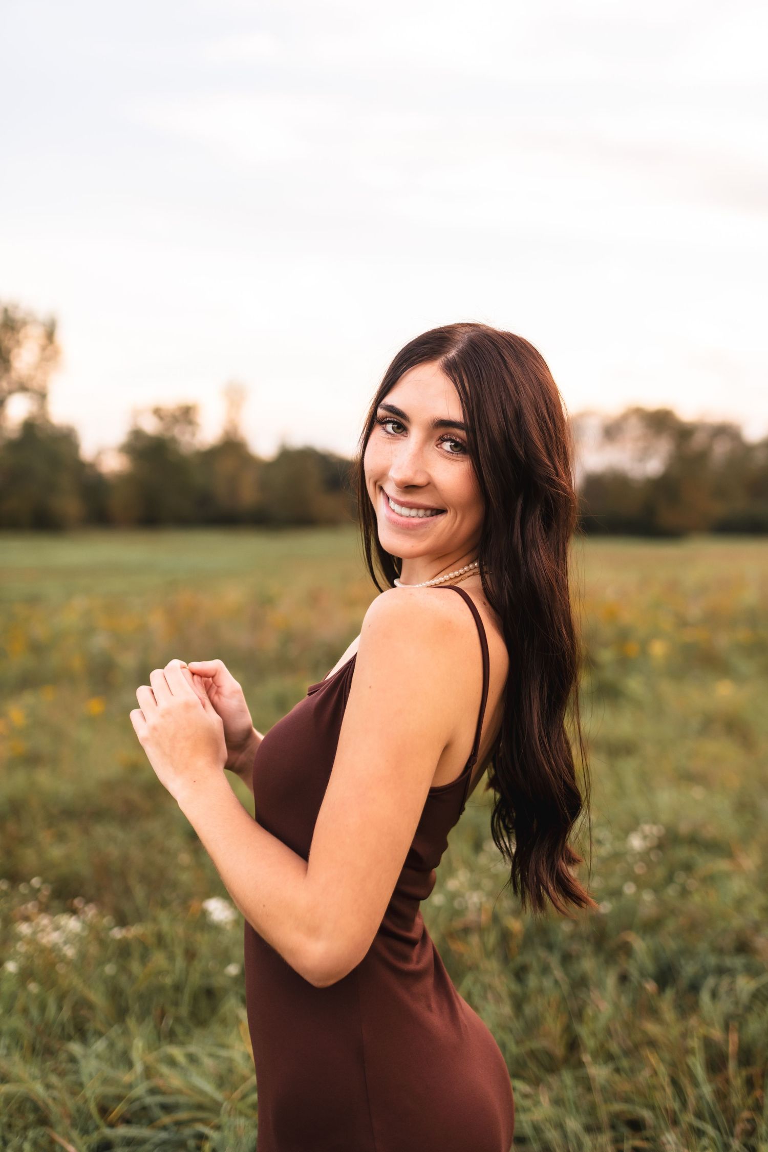 A senior portrait of a girl smiling at the camera in an open field.