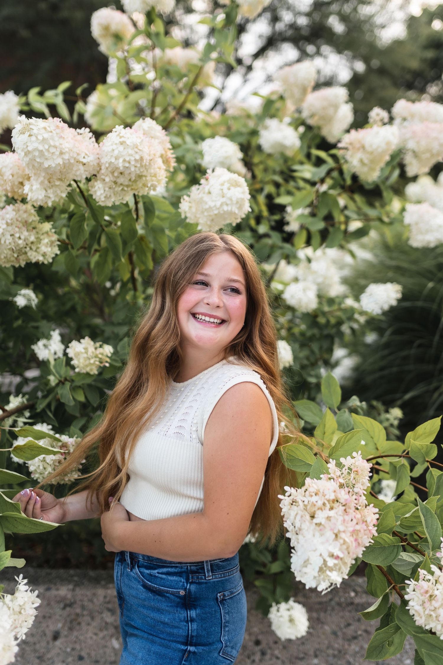 A portrait of a senior girl laughing in front of tall white flowers.