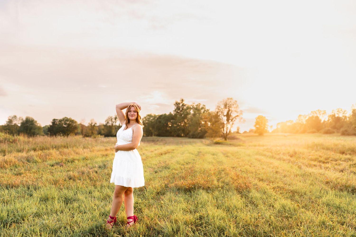A portrait of a senior in an open field, with the golden hour glow lighting up the grass.