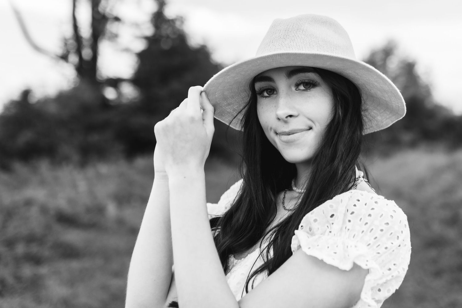 A black and white portrait of a senior holding her wide brim hat.