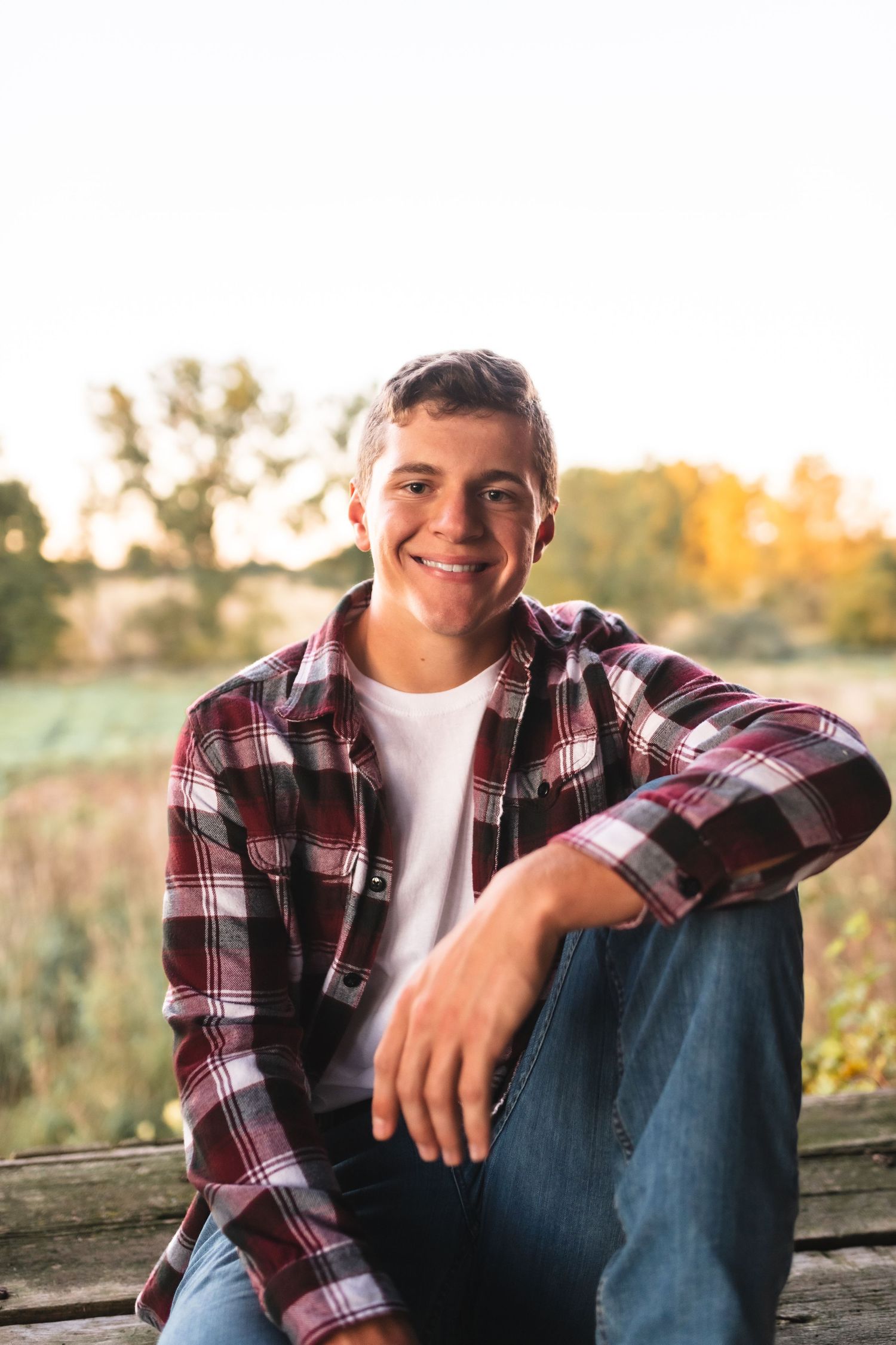 A senior boy smiling at the camera during a senior portrait session on his family farm.