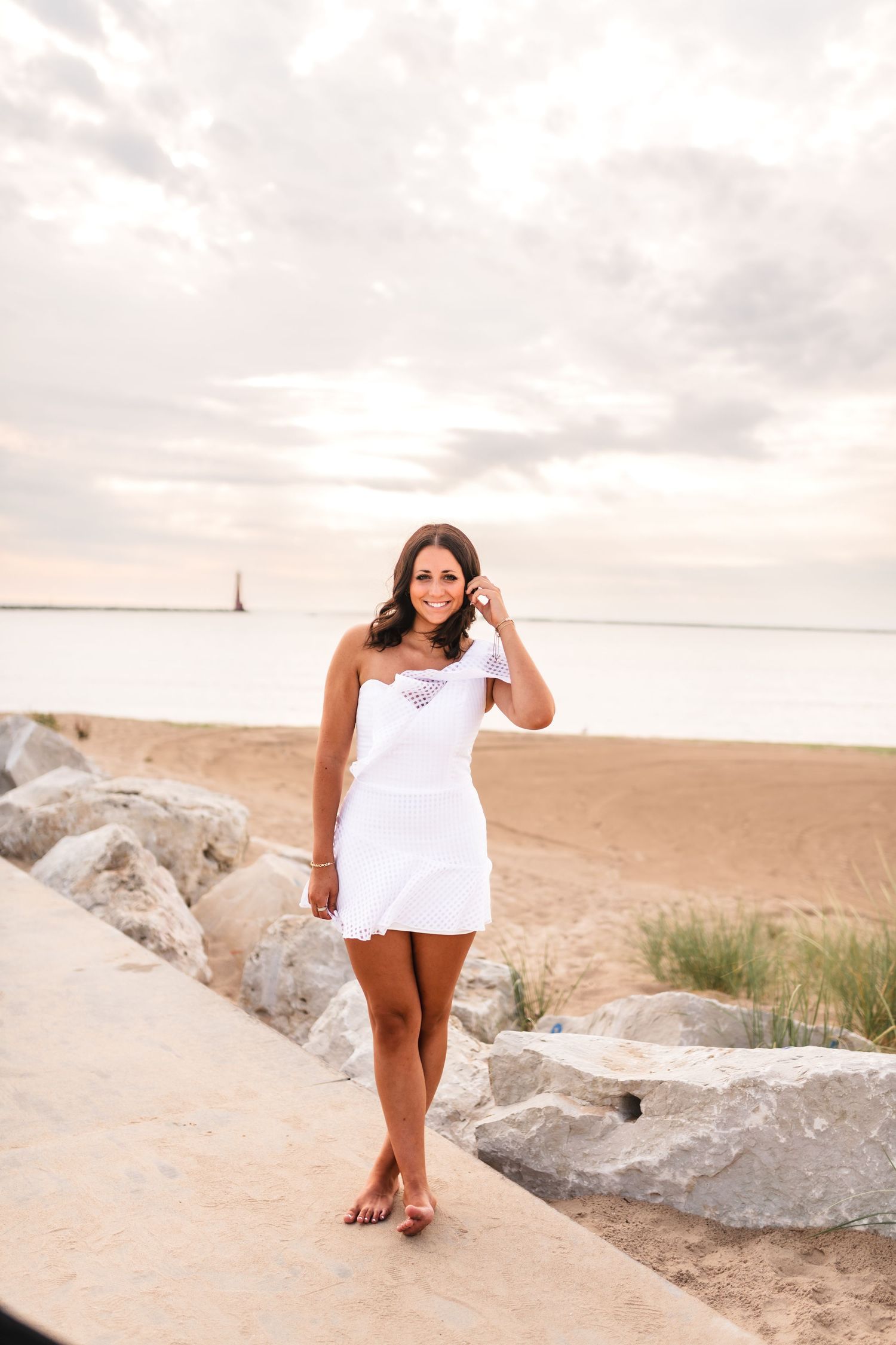 A girl during her senior photos in a tight white dress posing on the beach at Muskegon, MI.