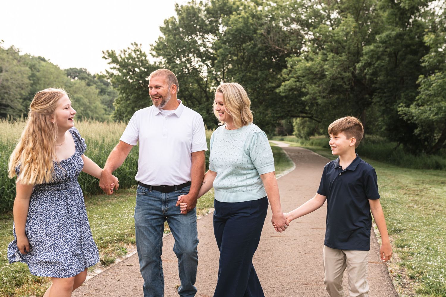 Candid photo of a family of four laughing at each other as they walk down a shaded path.
