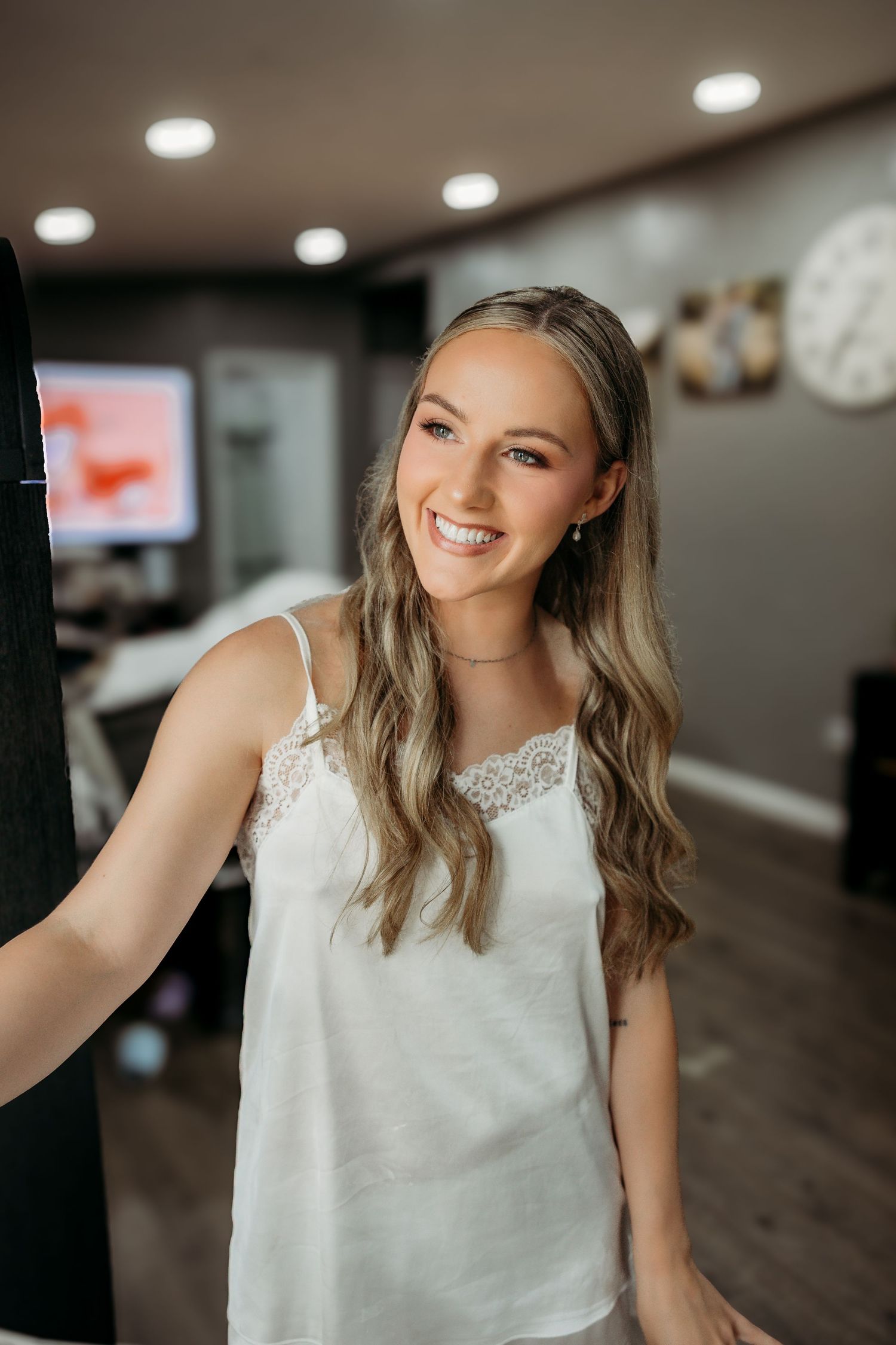 Woman wearing sleeveless white lace top smiles brightly in indoor setting with recessed lighting.
