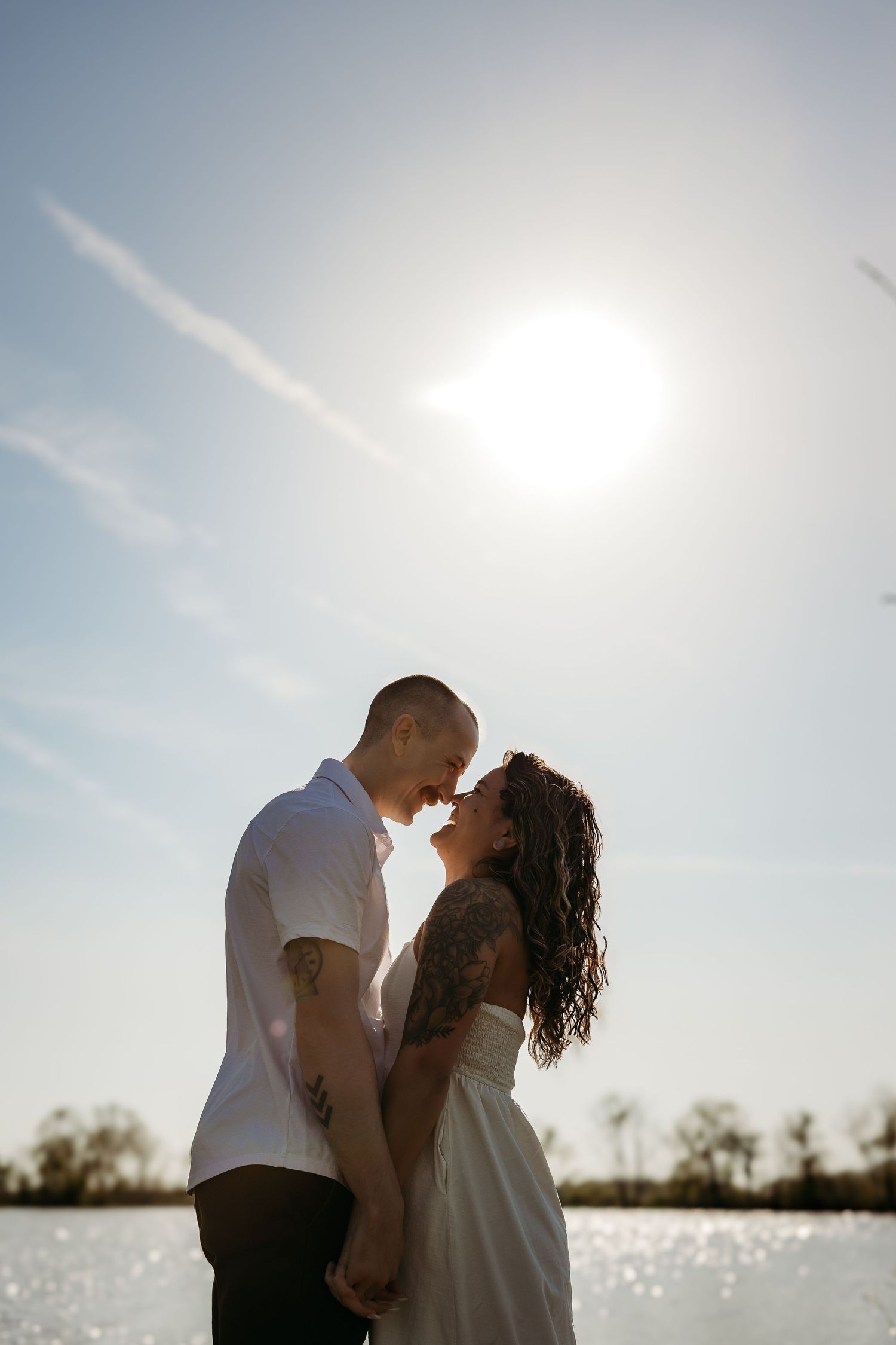 A romantic silhouette of a couple sharing an intimate moment by the water at sunset with sparkling reflections.