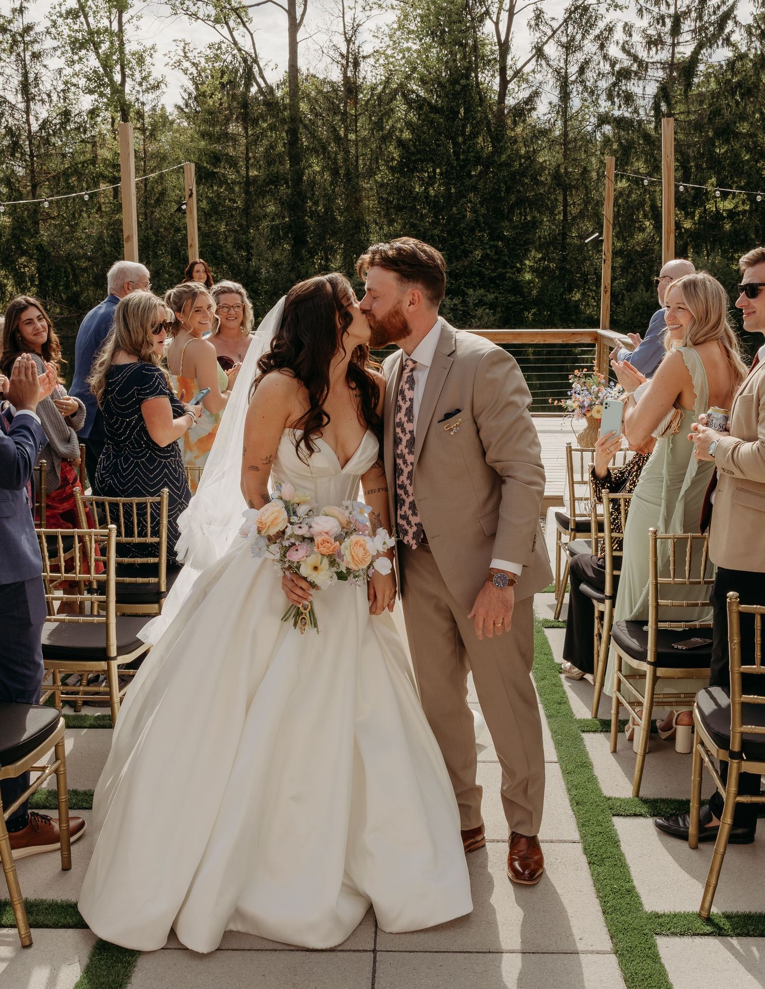 Newlyweds share first kiss as married couple walking down outdoor wedding ceremony aisle.