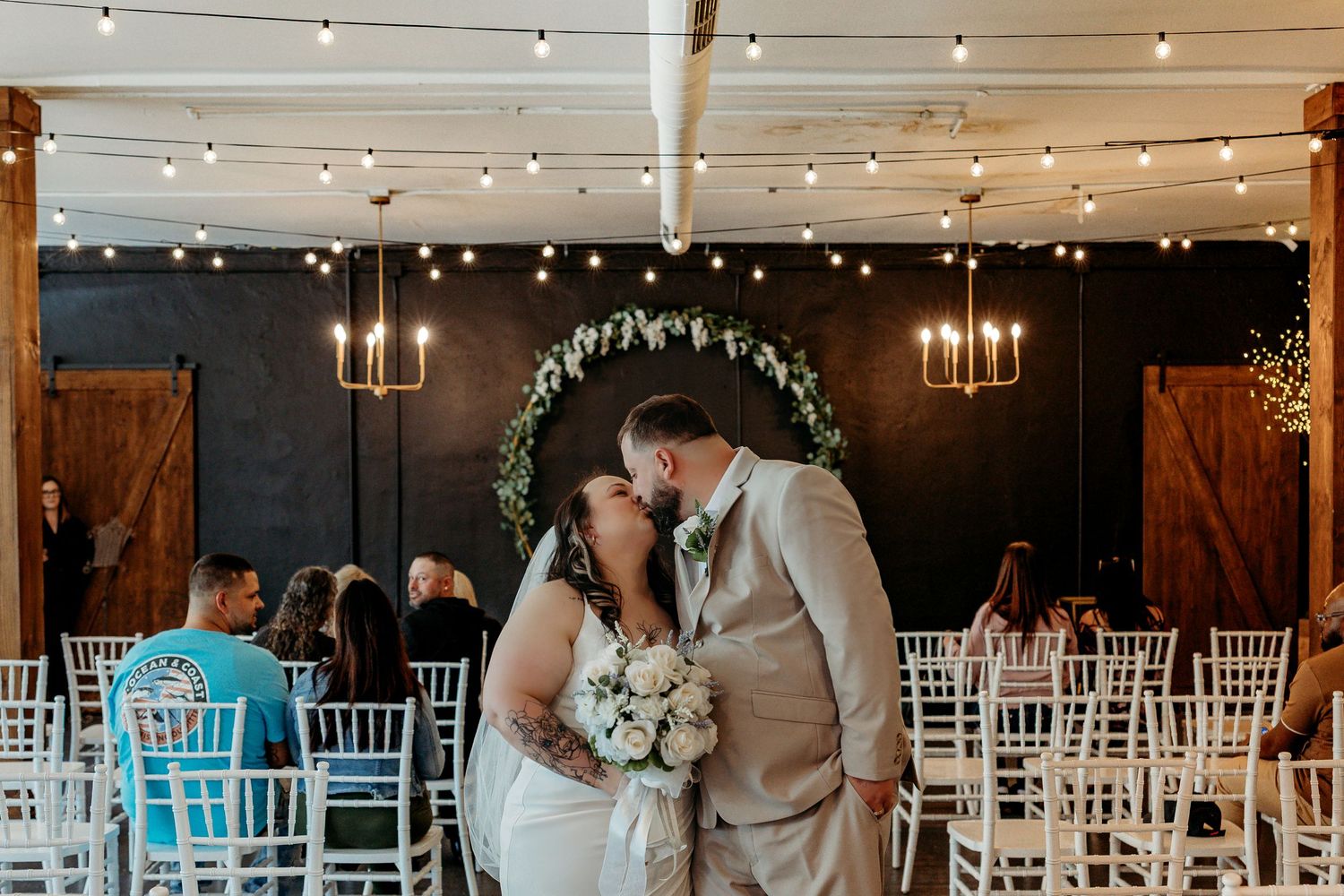 Romantic outdoor wedding reception setup at dusk with string lights illuminating elegant white chairs and tables.