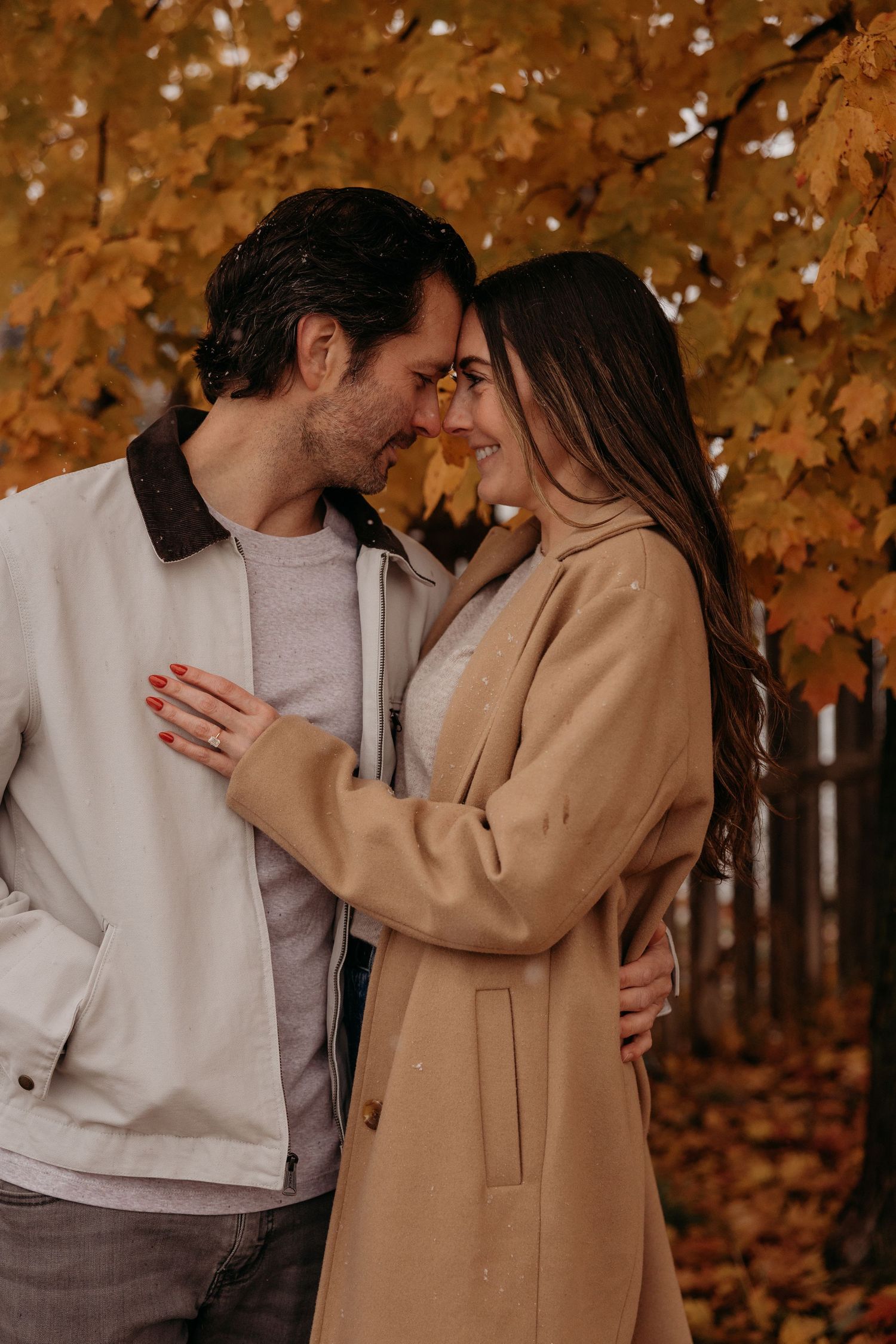 A romantic couple embraces in an autumn forest setting with golden leaves in the background.