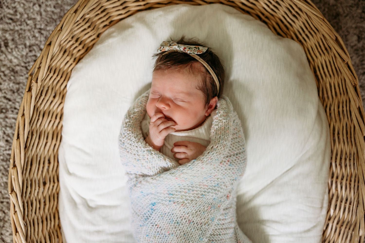 A newborn baby wrapped in a soft knit blanket sleeps peacefully in a round woven basket.