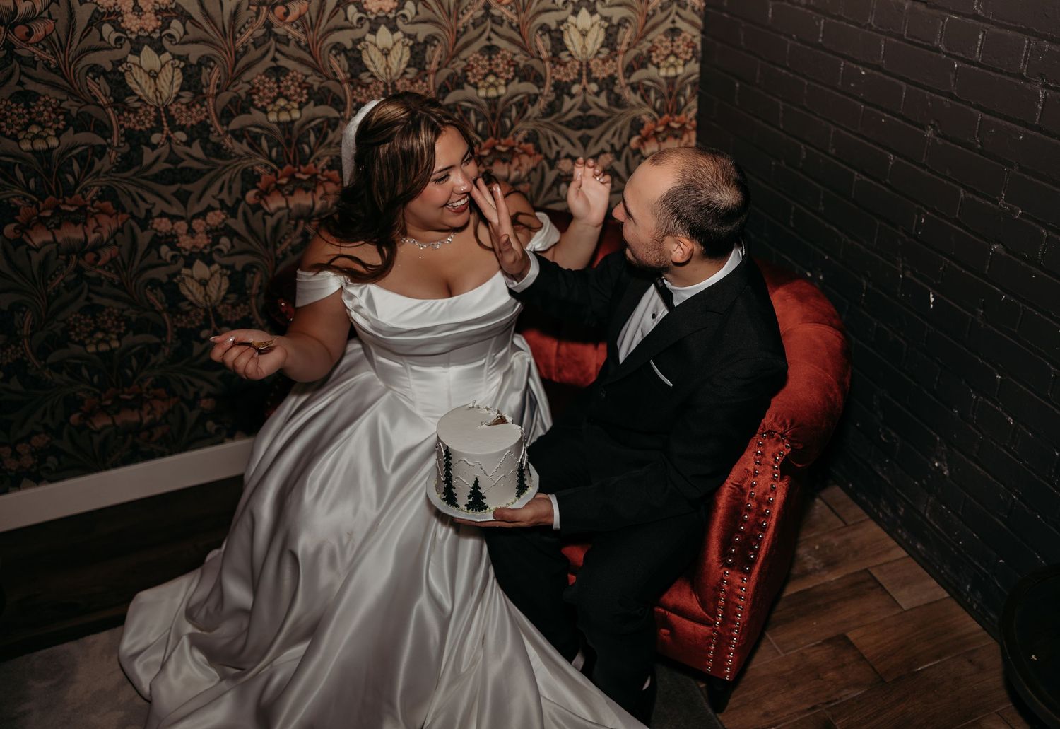 Bride and groom share a joyful moment feeding cake to each other in elegant wedding attire.