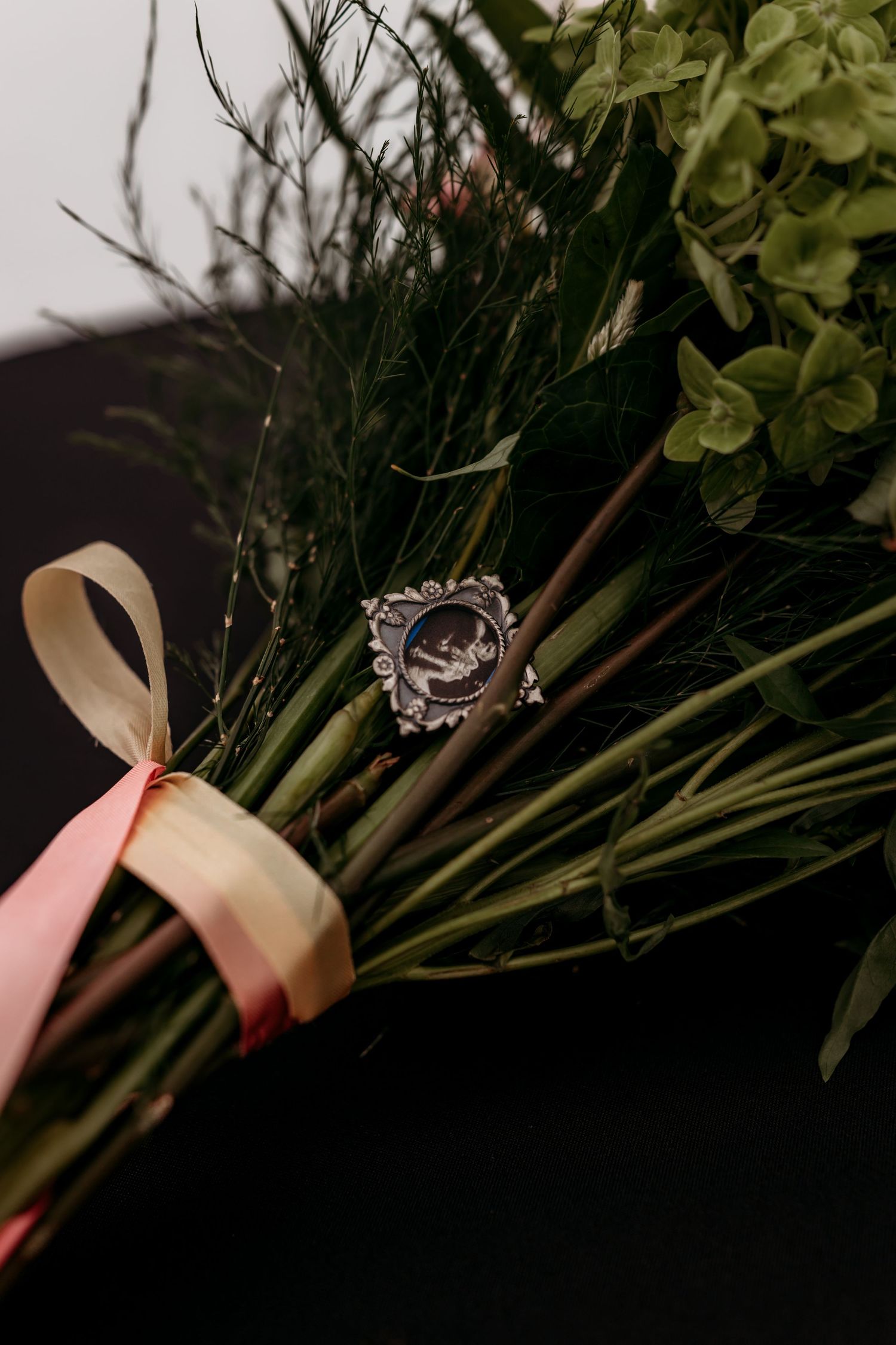 Antique silver ring displayed on a bouquet tied with pink and cream ribbons against a dark background.