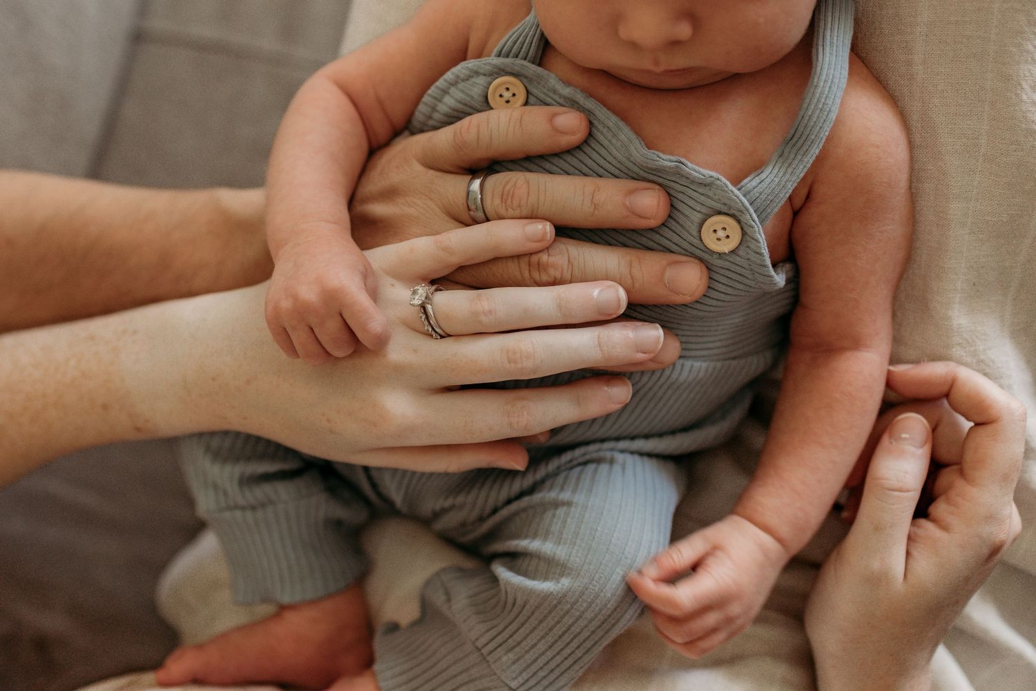 Gentle hands cradle an infant wearing a soft gray ribbed outfit in a heartwarming close-up moment.