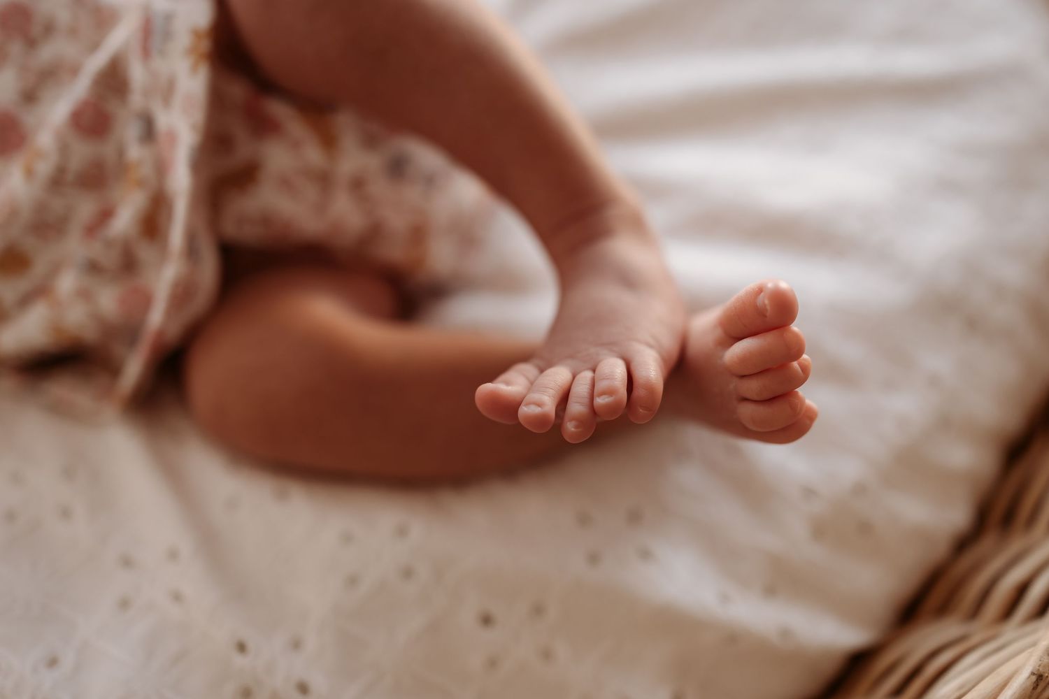 Close-up view of tiny baby feet and hands resting on white textured bedding.