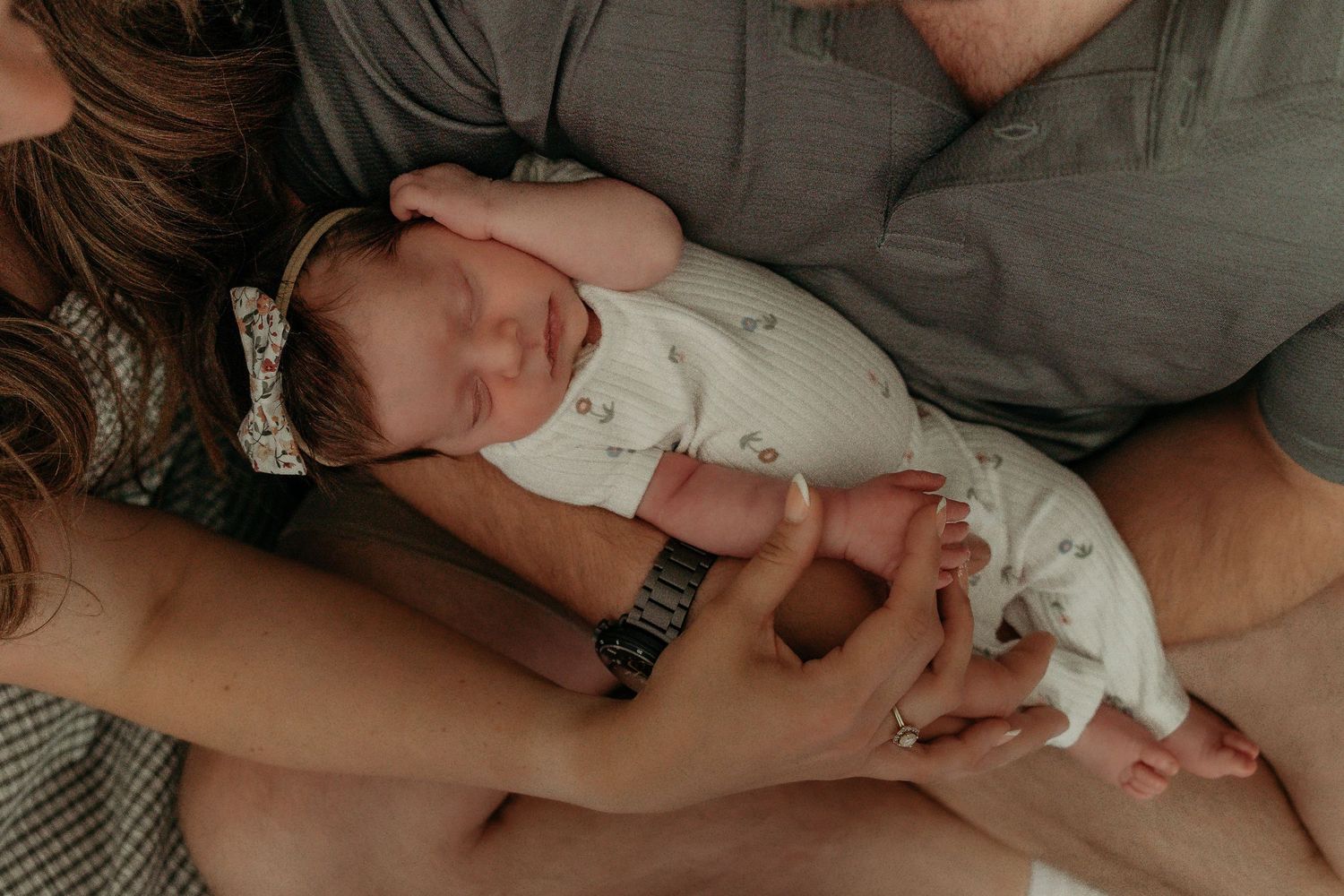 A tiny newborn baby in white onesie sleeps peacefully while being cradled in caring hands.