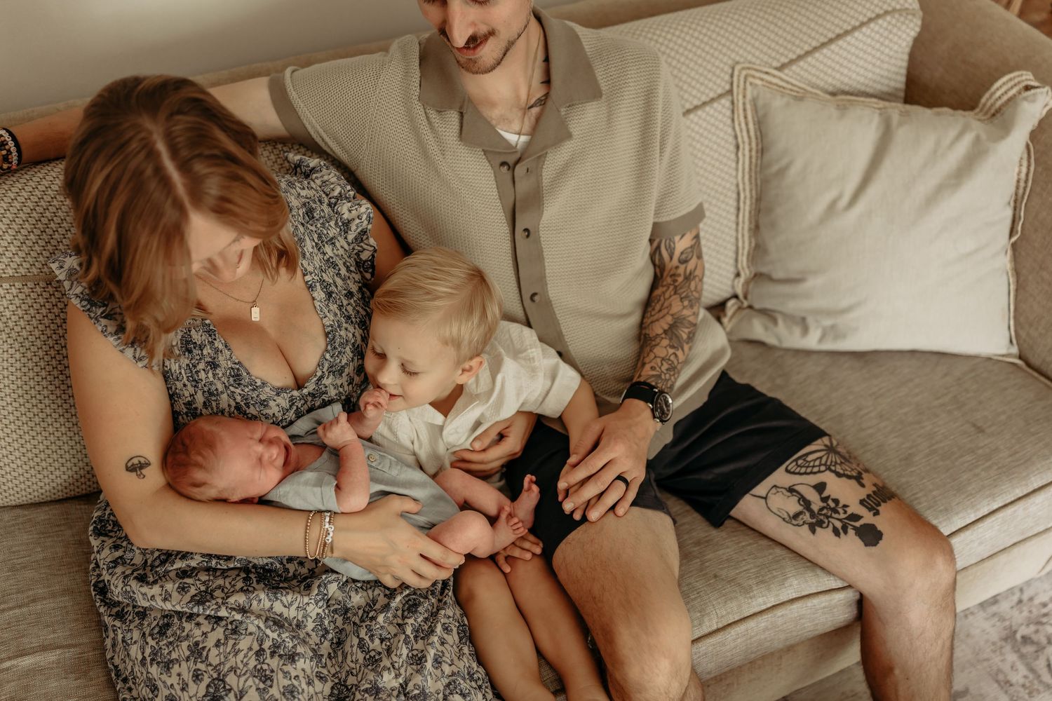 Tender family moment photographed in muted tones on a beige couch with natural window lighting.