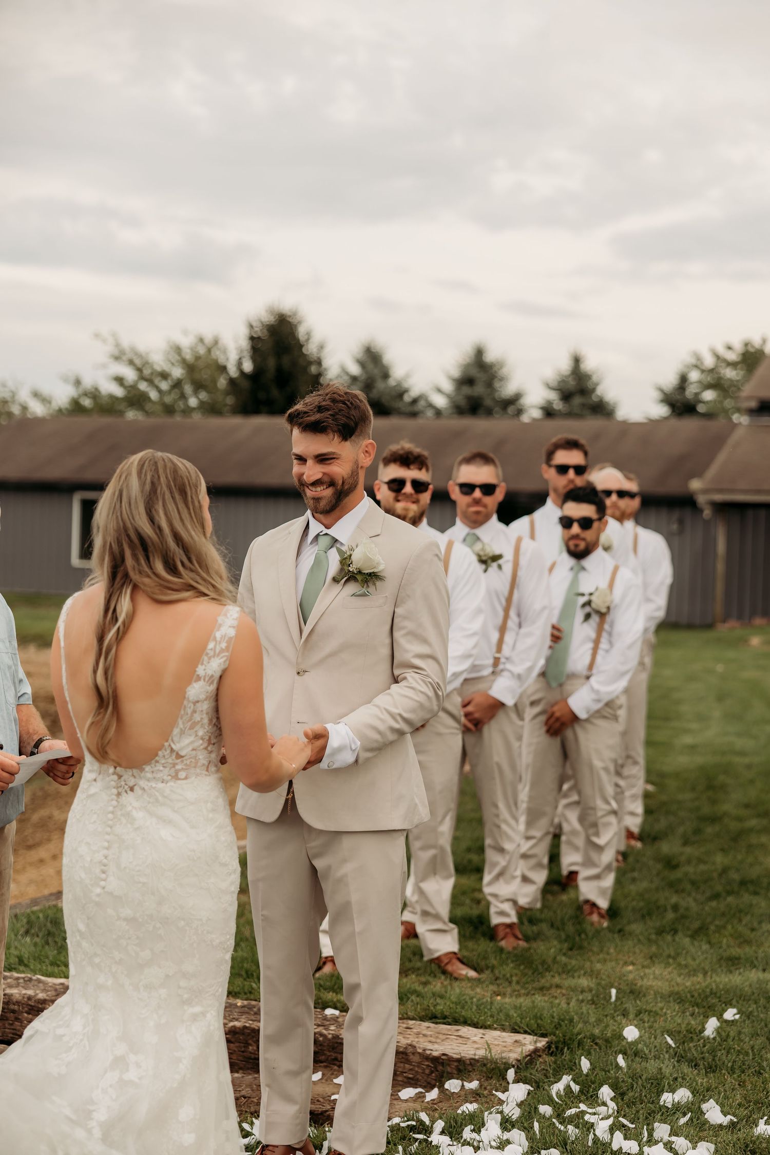 Wedding party groomsmen in khaki suits and white shirts line up outdoors in a grassy field during a summer celebration.