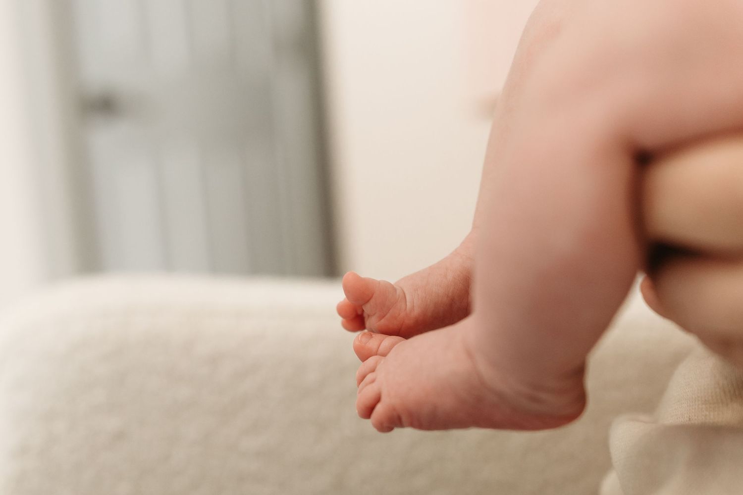 Close-up of a tiny baby foot resting on soft white fabric shows delicate toes and smooth infant skin.
