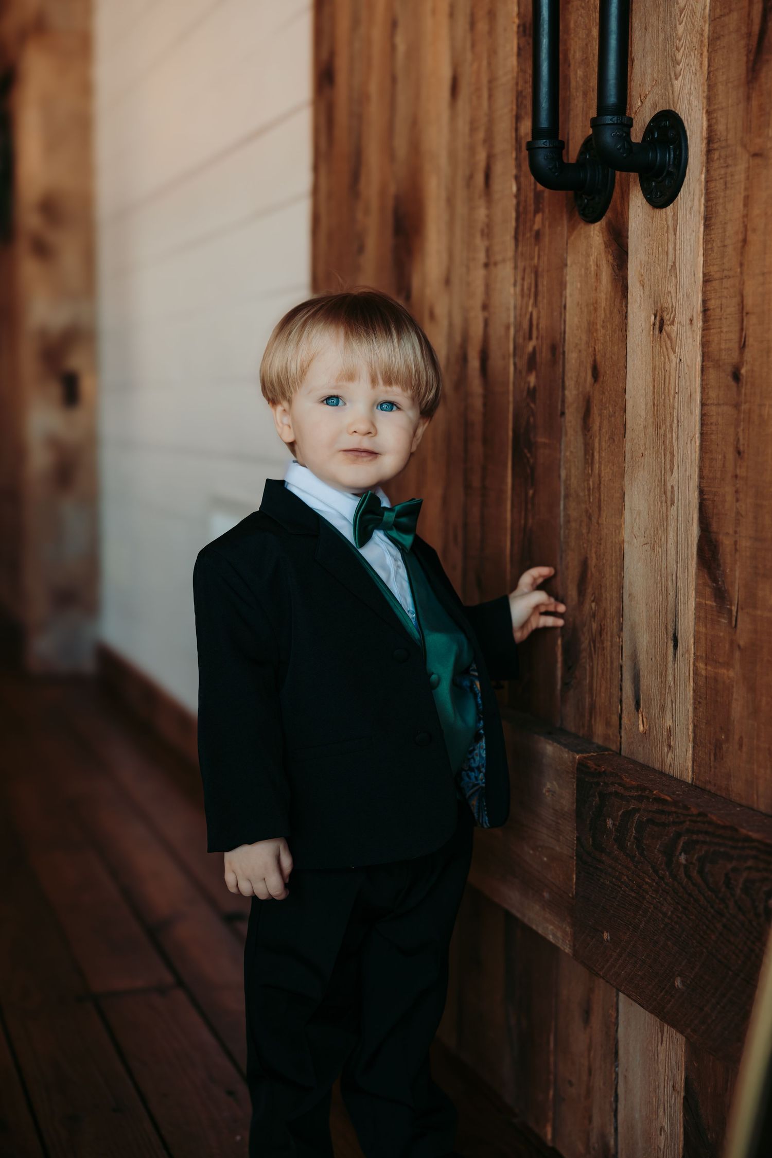 Young boy in a dark suit stands against rustic wooden paneling in a series of candid photo moments.