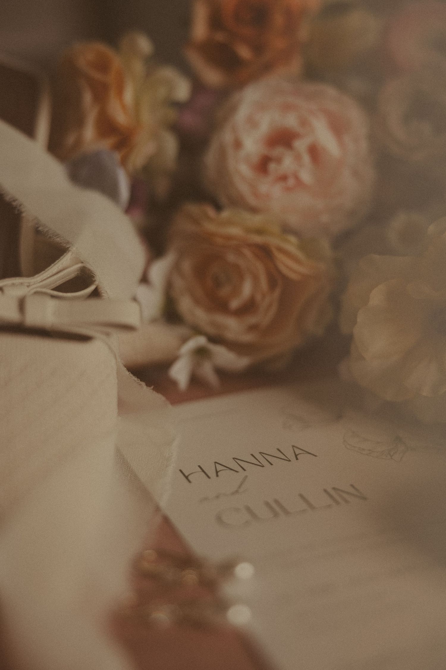 Elegant wedding stationery with names Hanna and Cullin surrounded by soft pink and peach roses in a romantic flat lay.