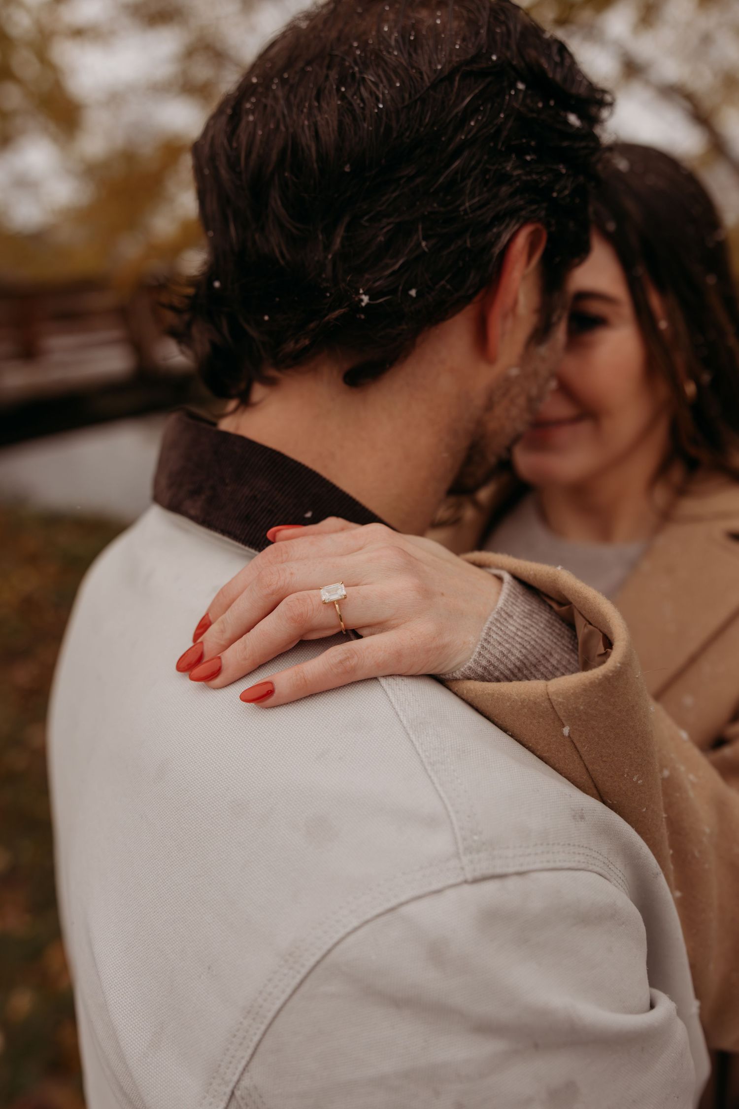 A romantic embrace captured in autumn showing hands with red nail polish resting on a shoulder.