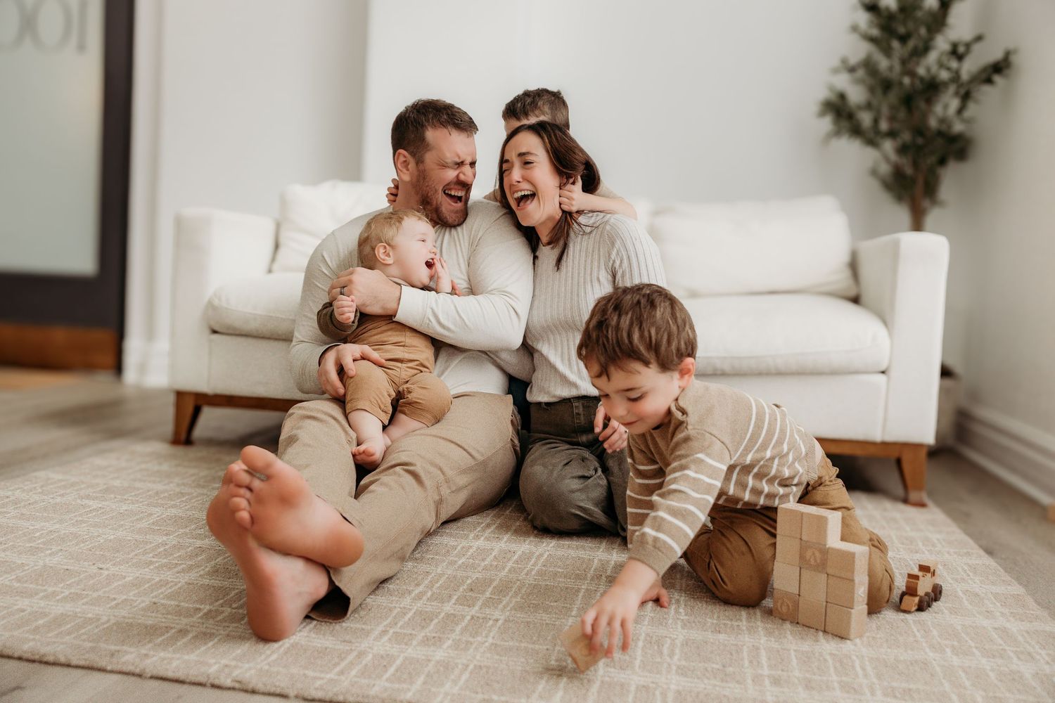 Family enjoying playful moment together on floor of minimalist living room with white sofa and wooden blocks.