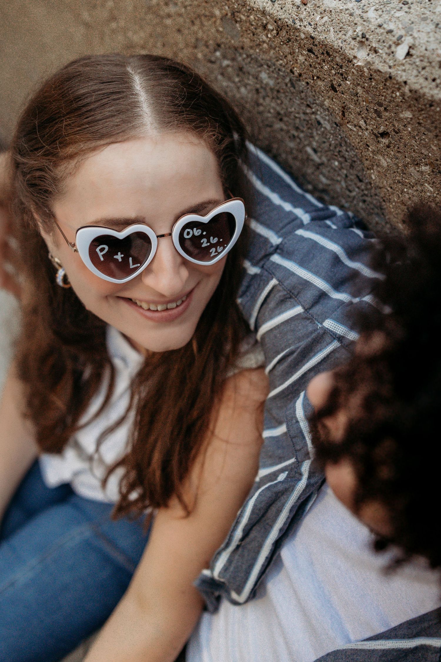 A person wearing heart-shaped sunglasses poses with a playful expression against a textured background.