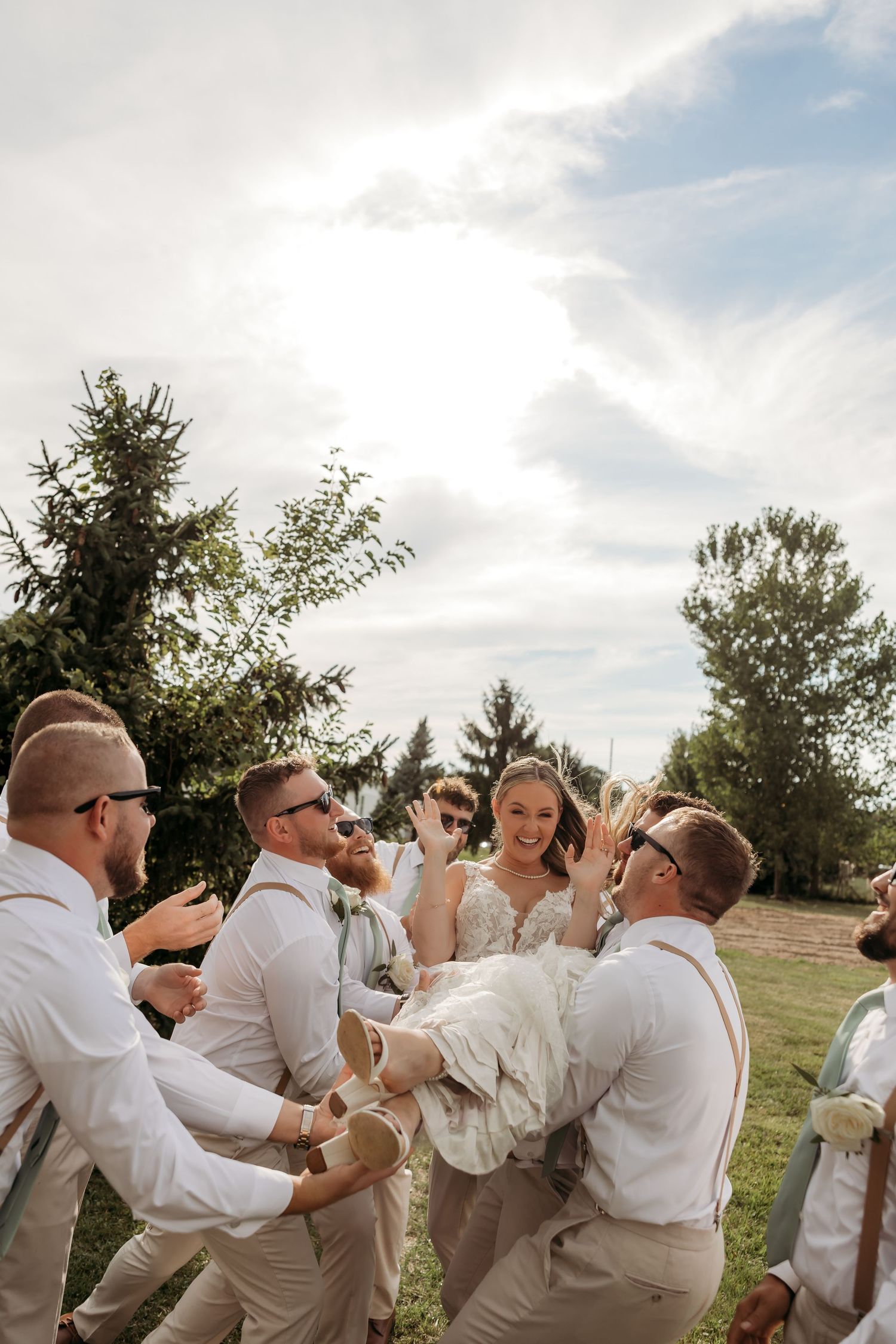 Wedding party celebrates joyfully outdoors with animated poses and laughter against a scenic natural backdrop.
