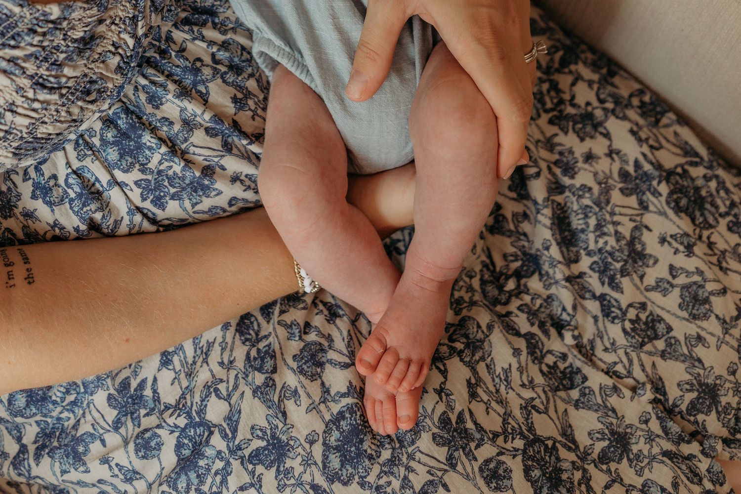 Tiny bare feet resting on blue and white floral bedding in soft natural light.