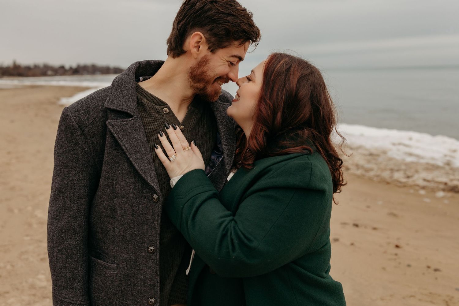A couple shares romantic moments together on a sandy beach during an overcast day.