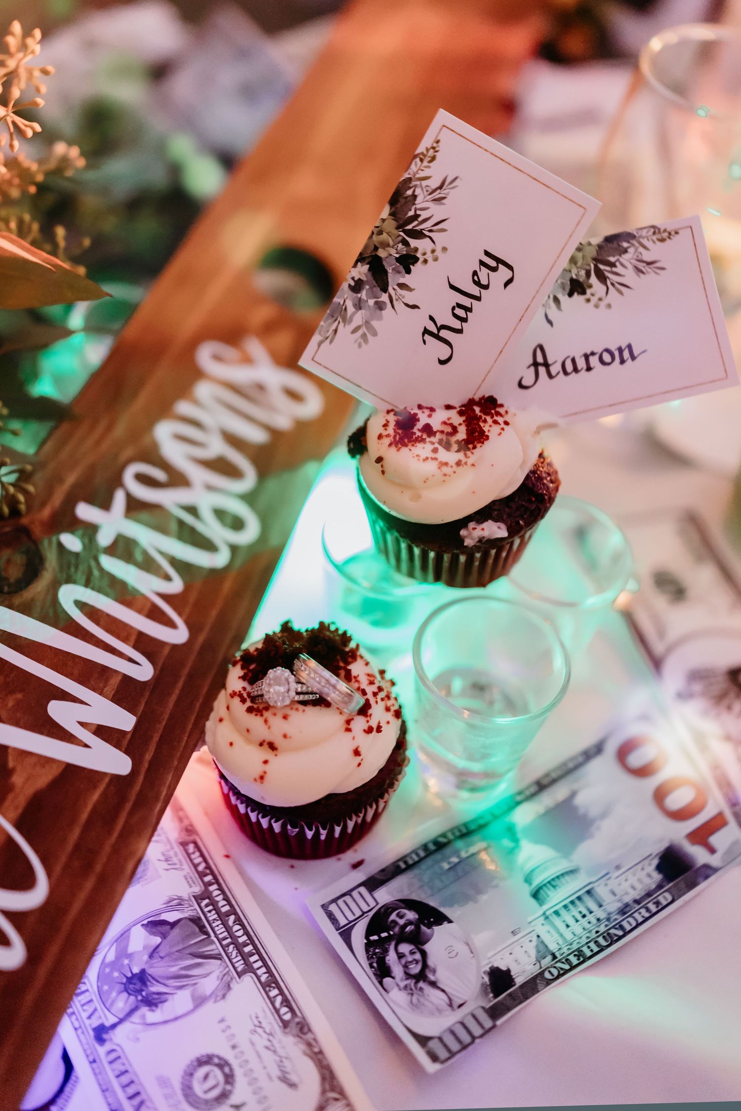 Wedding reception details showing place cards, cupcakes, and dollar bills under colorful mood lighting.