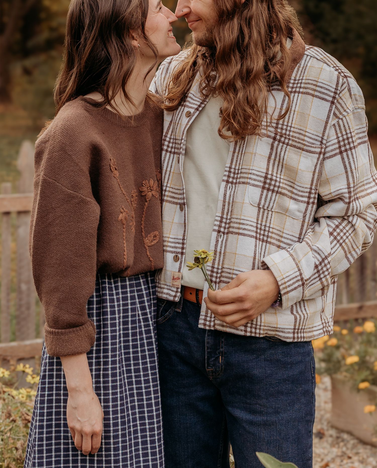 A couple in casual fall outfits sharing an intimate moment outdoors with autumn foliage in the background.