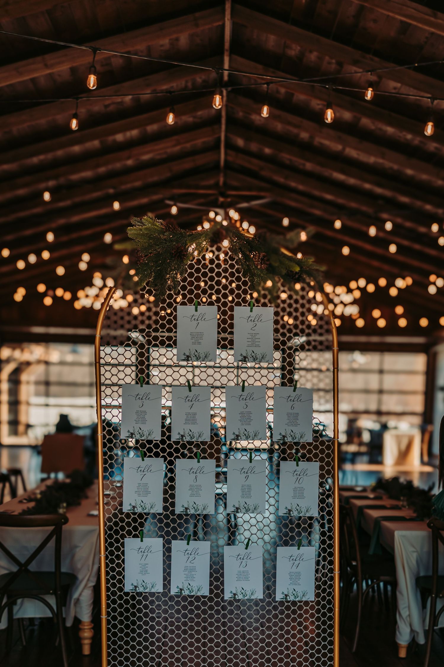 Wedding seating chart display with string lights in rustic barn venue featuring glowing edison bulbs overhead.