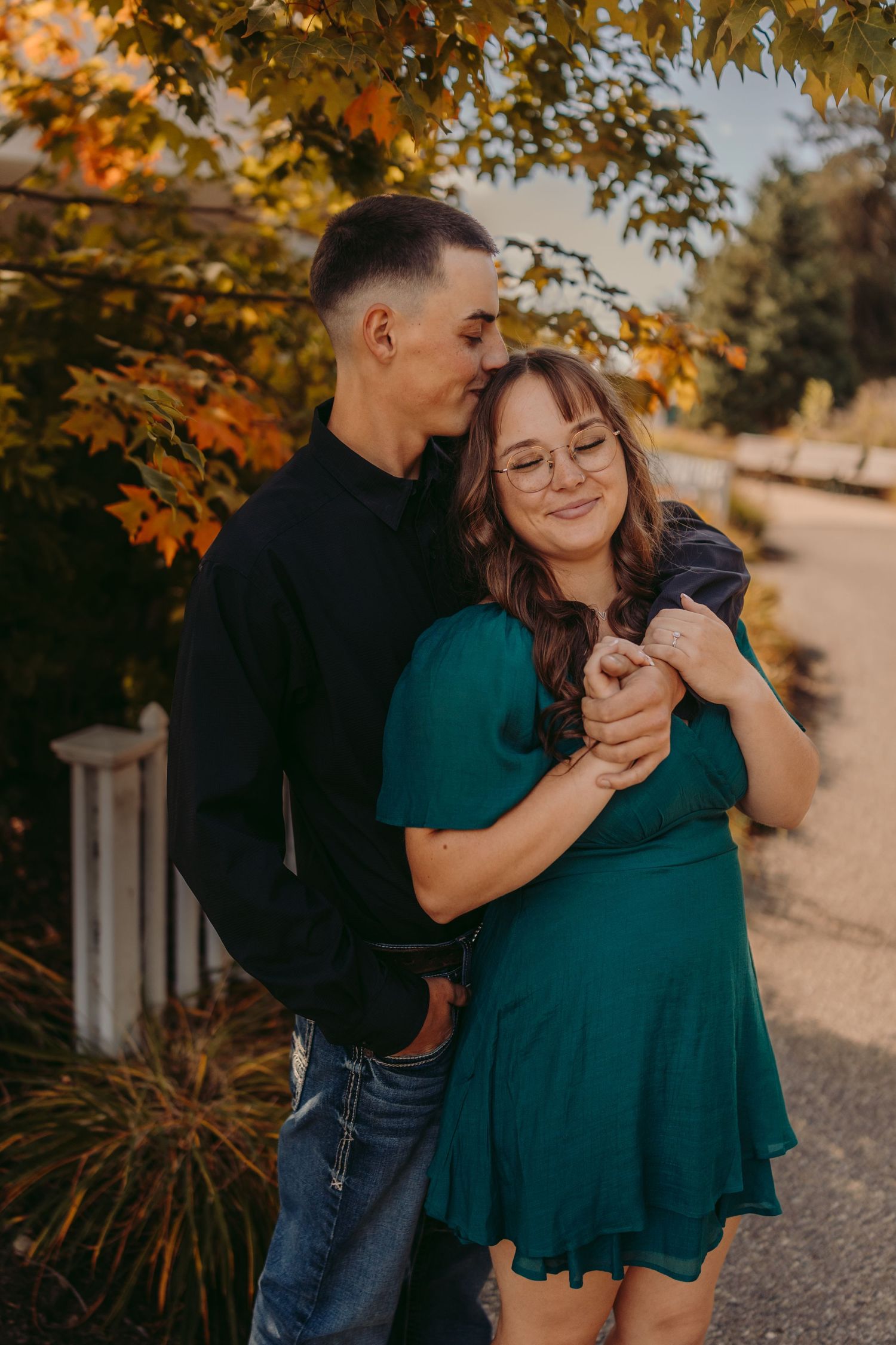 A couple embraces under autumn trees with golden leaves during a romantic outdoor photoshoot at sunset.