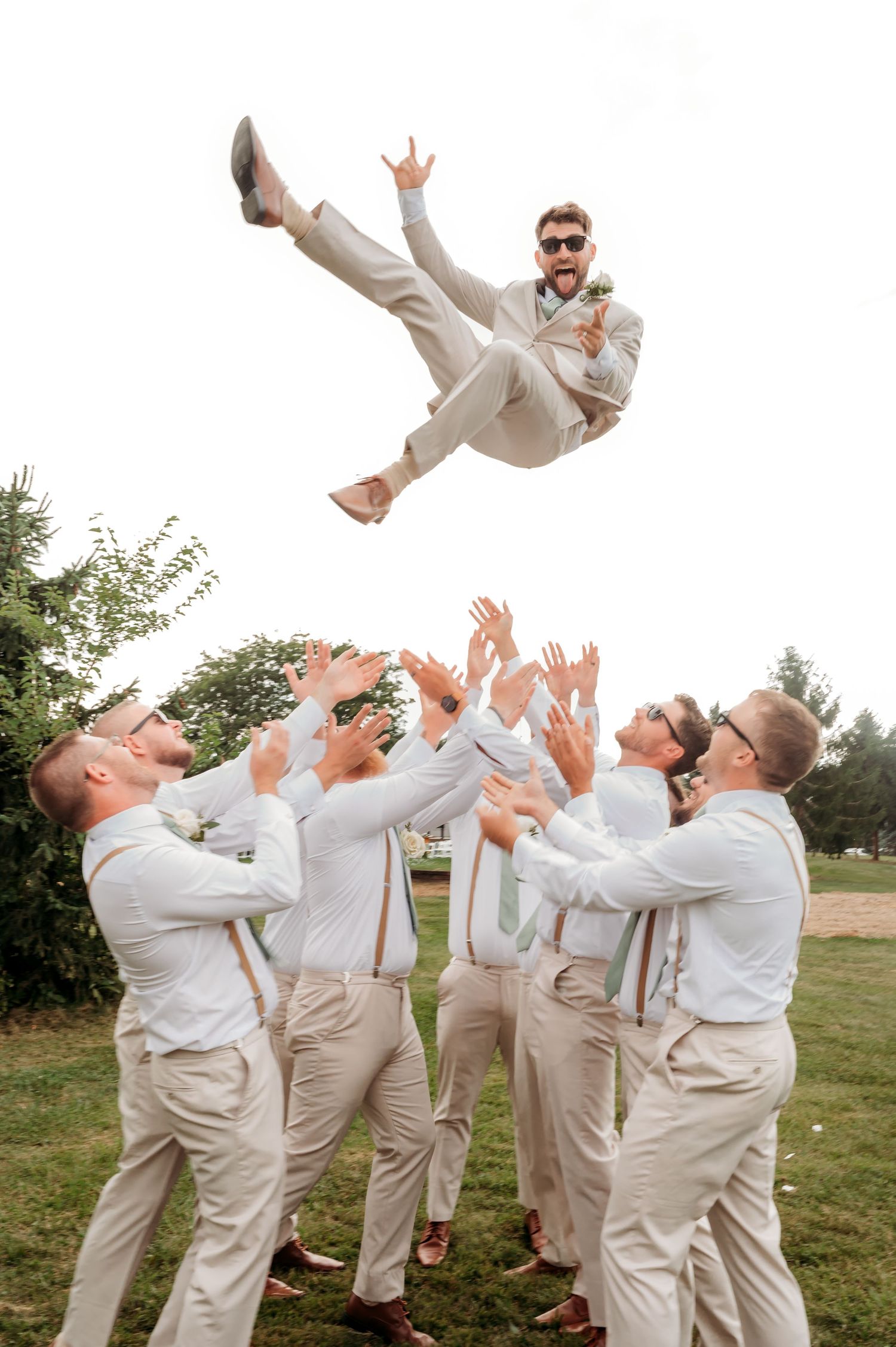 Groomsmen playfully toss another member of the wedding party into the air during outdoor photo session.