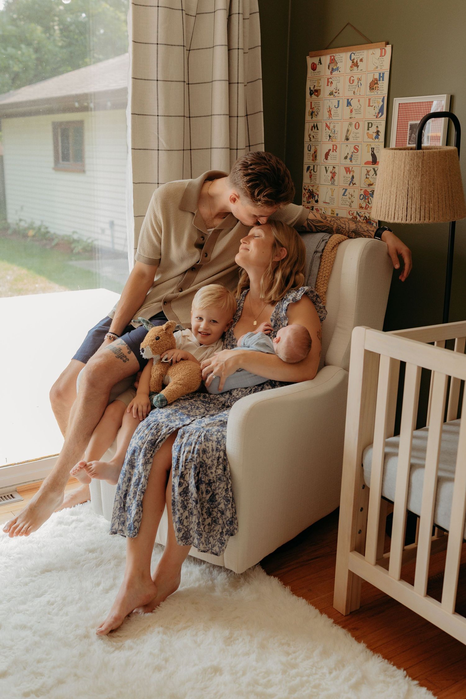 A tender moment shared between a couple and their baby relaxing together on a cozy armchair in a sunlit nursery.