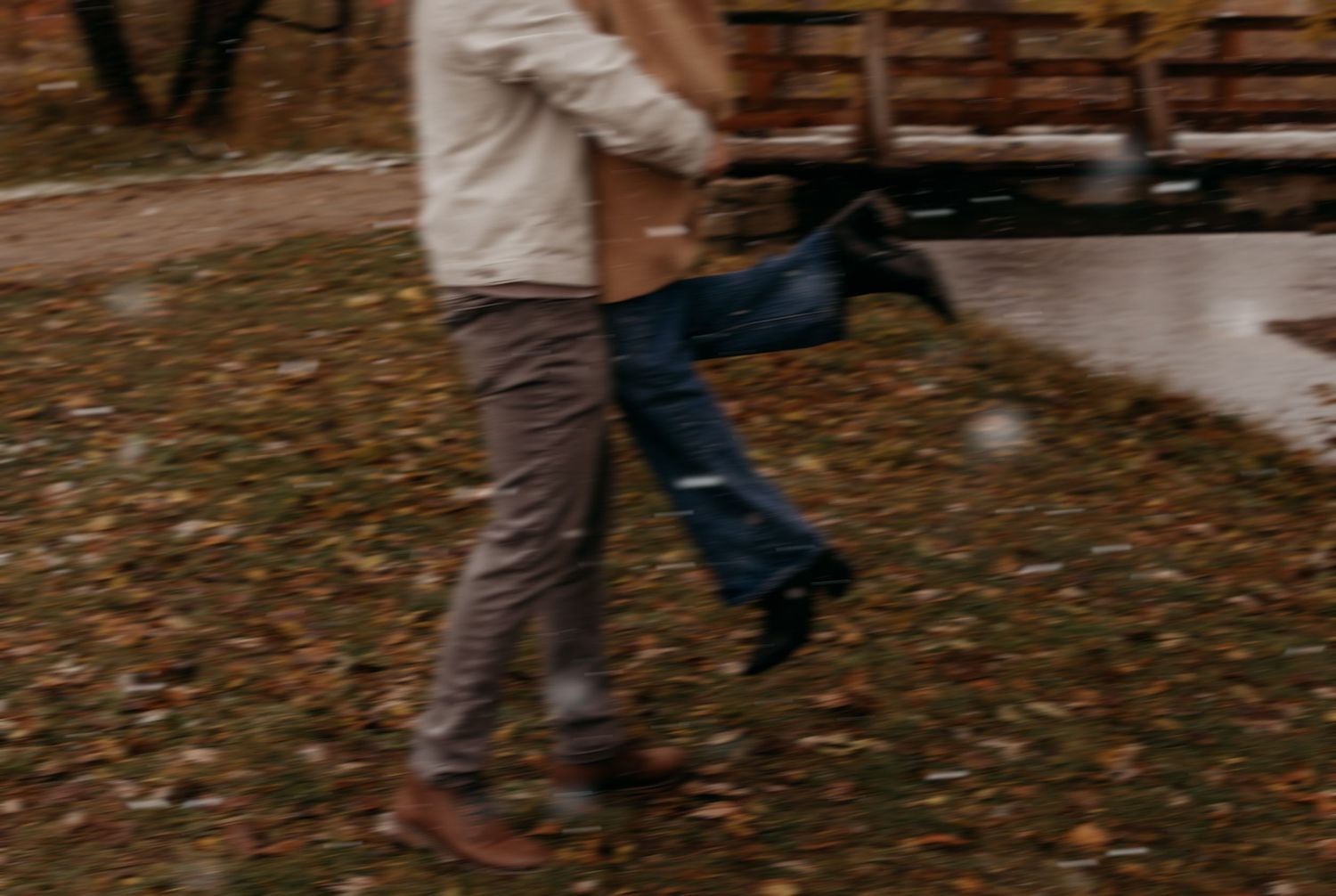 Person walking through fallen autumn leaves on wet pavement during a rainy day.